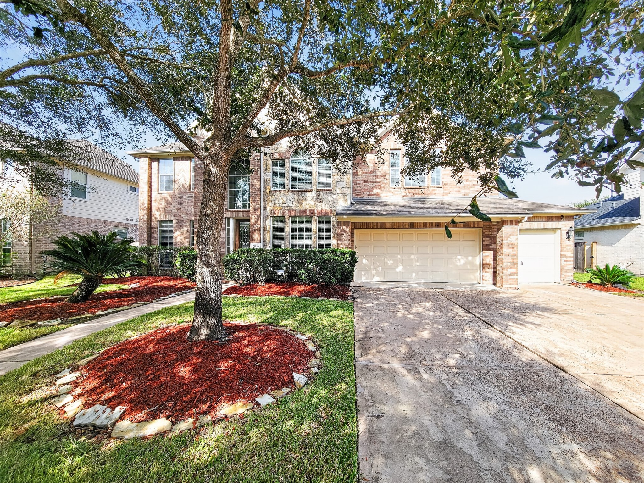 Charming two-story brick home with a spacious two-car garage, surrounded by mature trees and manicured landscaping, offering great curb appeal.