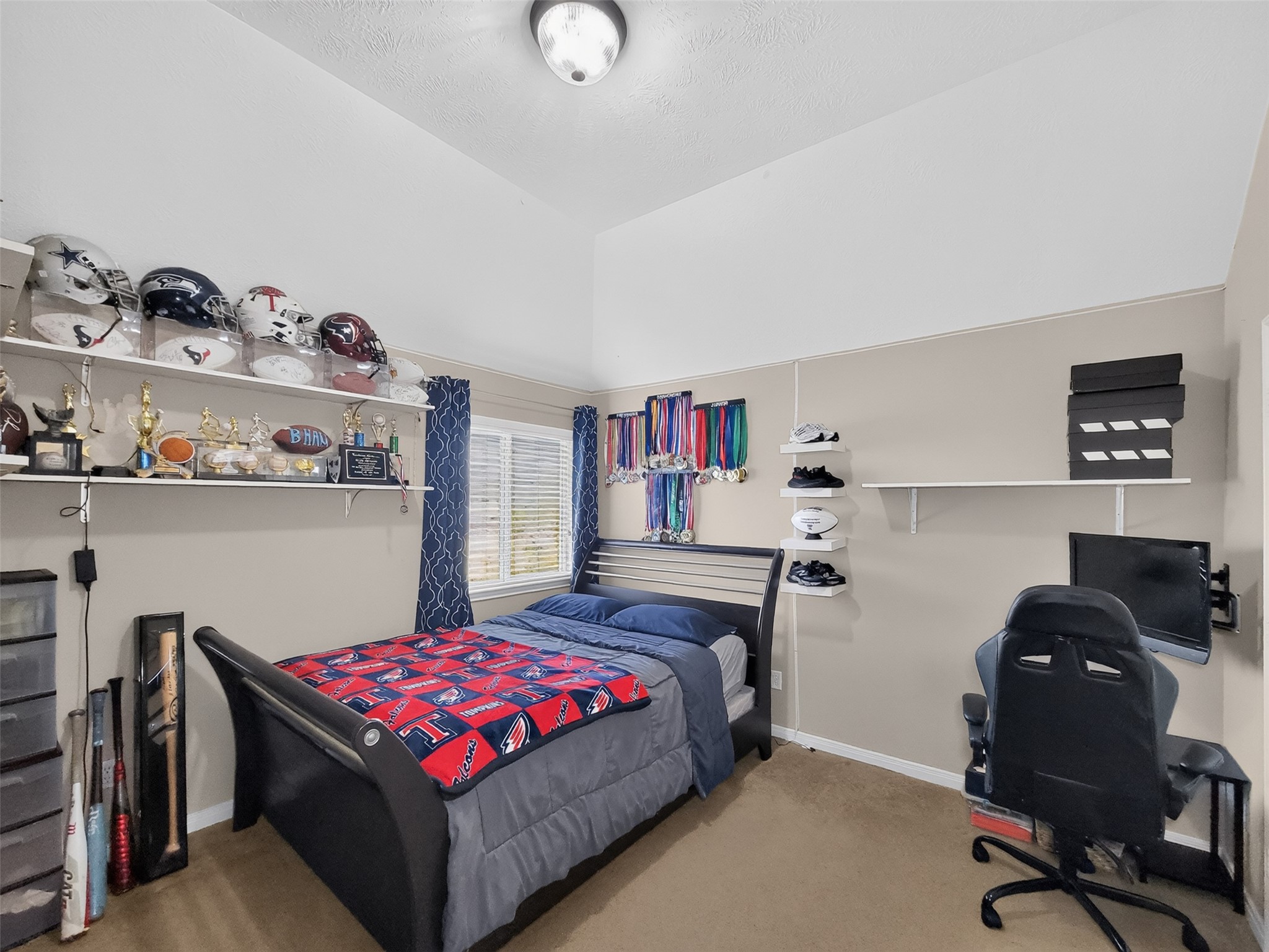 Cozy bedroom with sloped ceiling, featuring a comfortable bed, ample shelving for trophies and memorabilia, and a study area with a desk and chair, perfect for a young sports enthusiast.