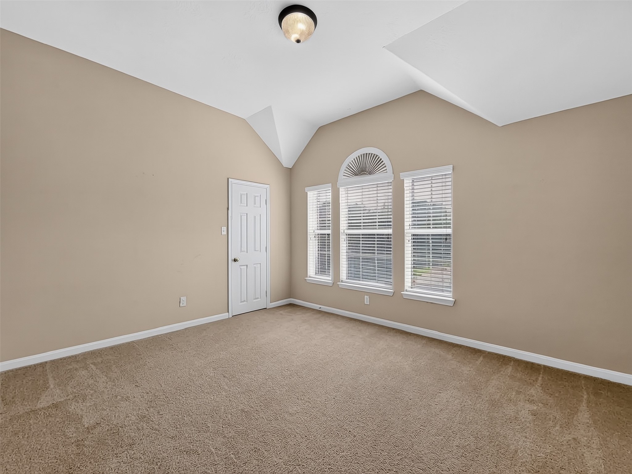 Spacious bedroom with vaulted ceilings, abundant natural light from large arched windows, and warm neutral tones.