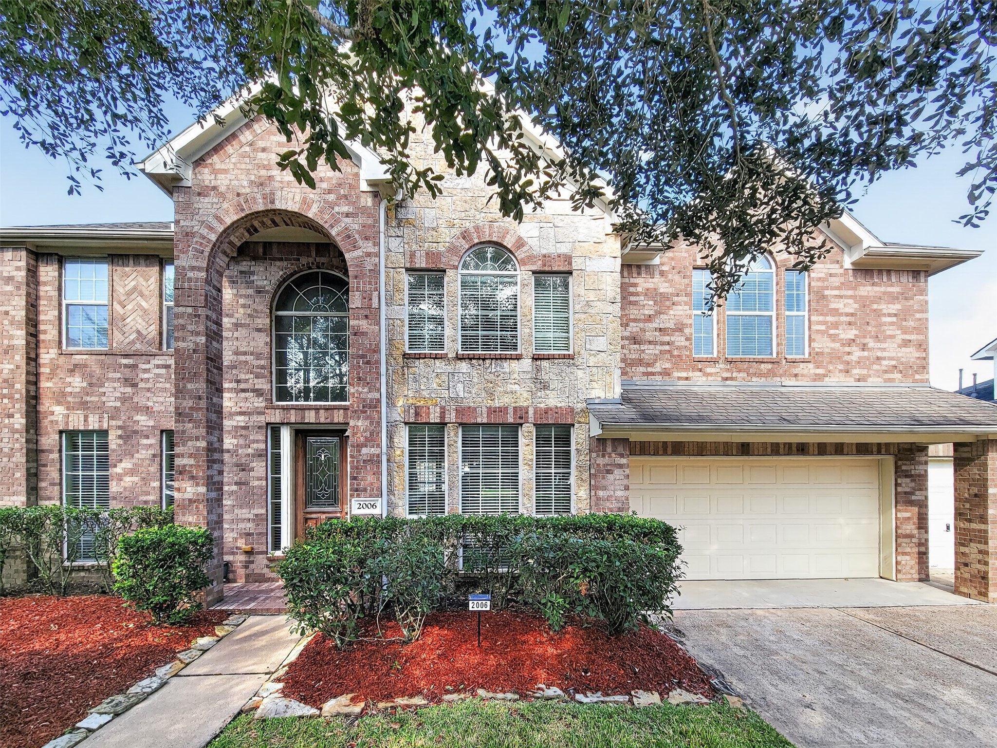Stunning two-story brick home featuring elegant archways, large windows, and a welcoming entrance, complemented by a spacious two-car garage and well-maintained landscaping.
