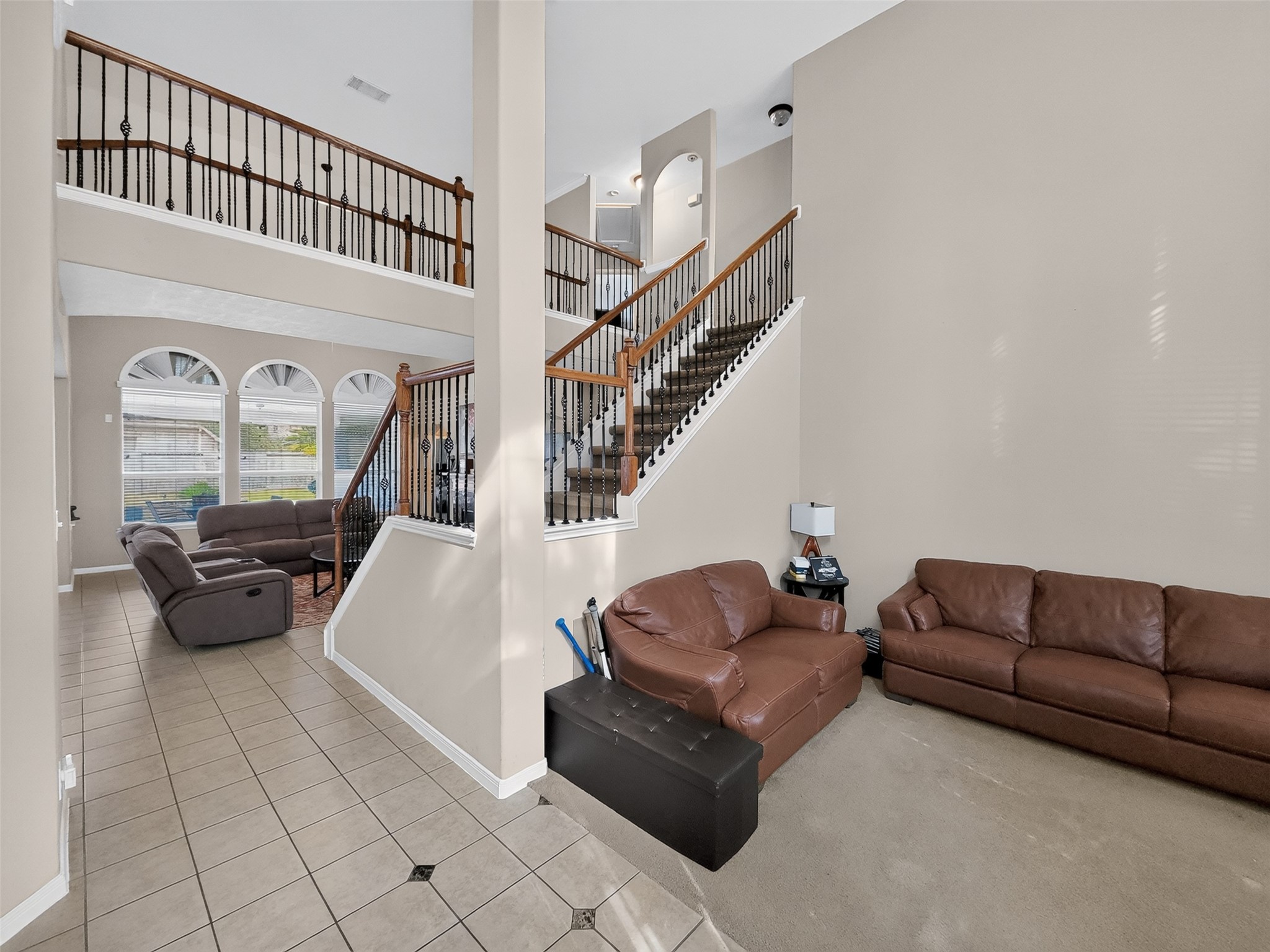 Spacious living area with high ceilings, elegant staircase, and abundant natural light from large arched windows, perfect for both relaxation and entertaining.