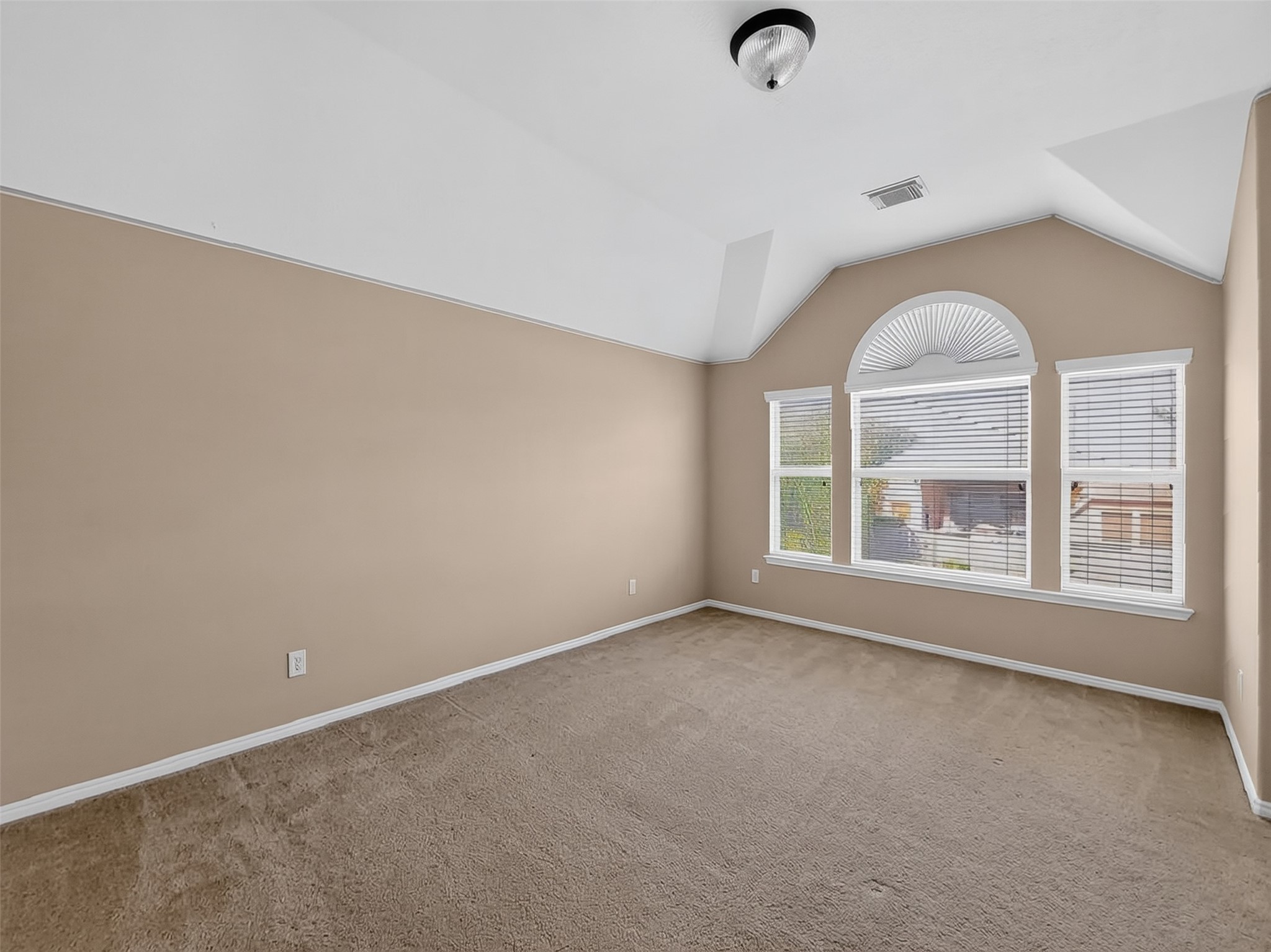 Spacious room with vaulted ceiling, featuring a large arched window that fills the space with natural light.