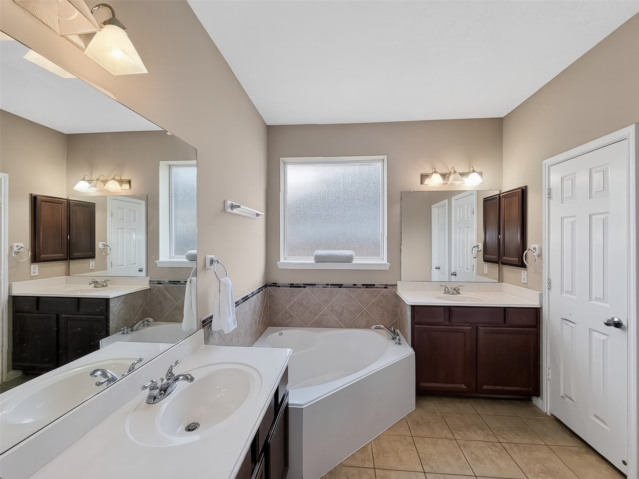 Elegant bathroom featuring a spacious corner soaking tub, dual sinks with ample counter space, and rich dark wood cabinetry, complemented by soft lighting and tiled flooring.