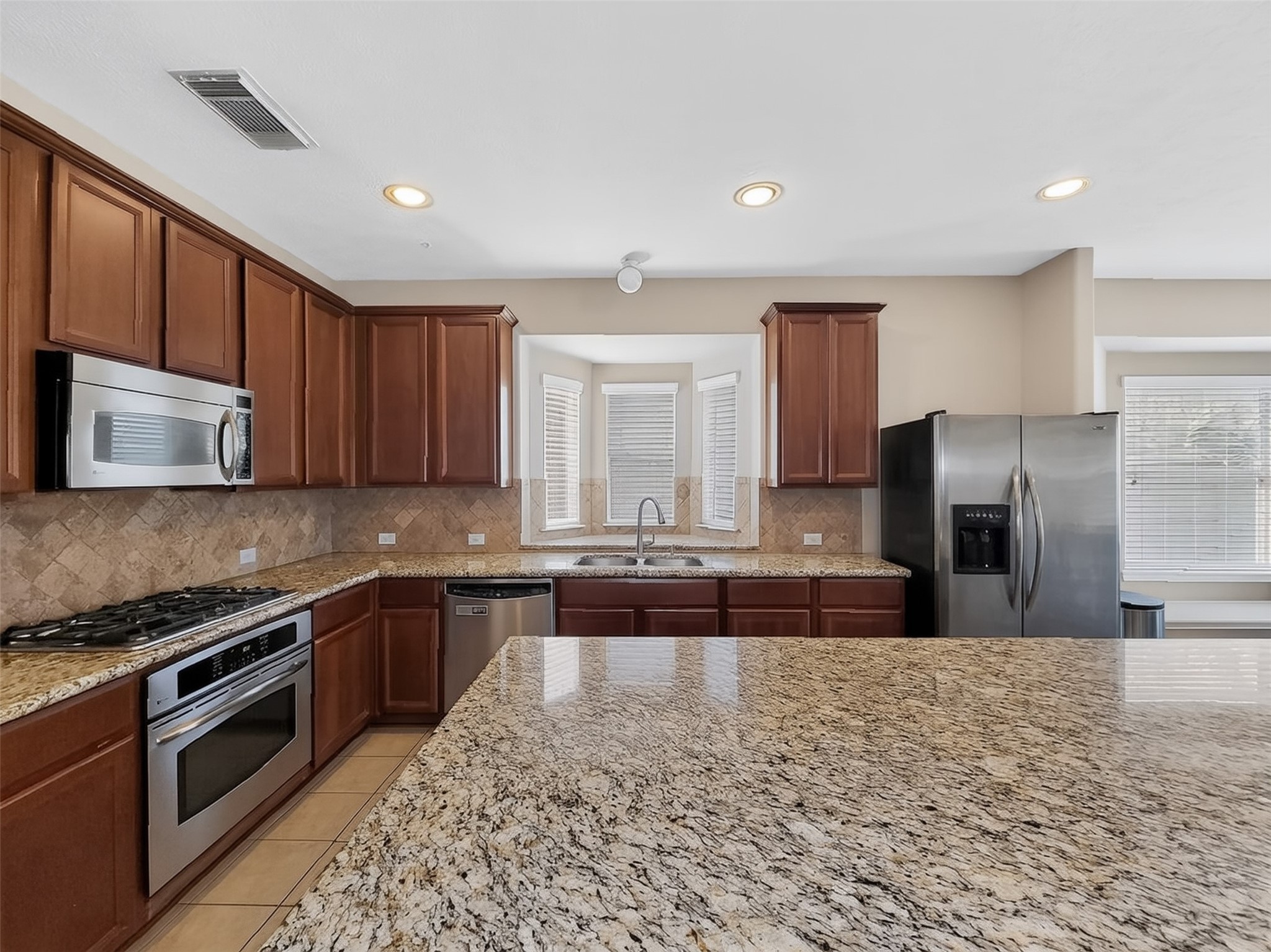 Spacious kitchen featuring elegant granite countertops, stainless steel appliances, and rich wood cabinetry, perfect for culinary enthusiasts.
