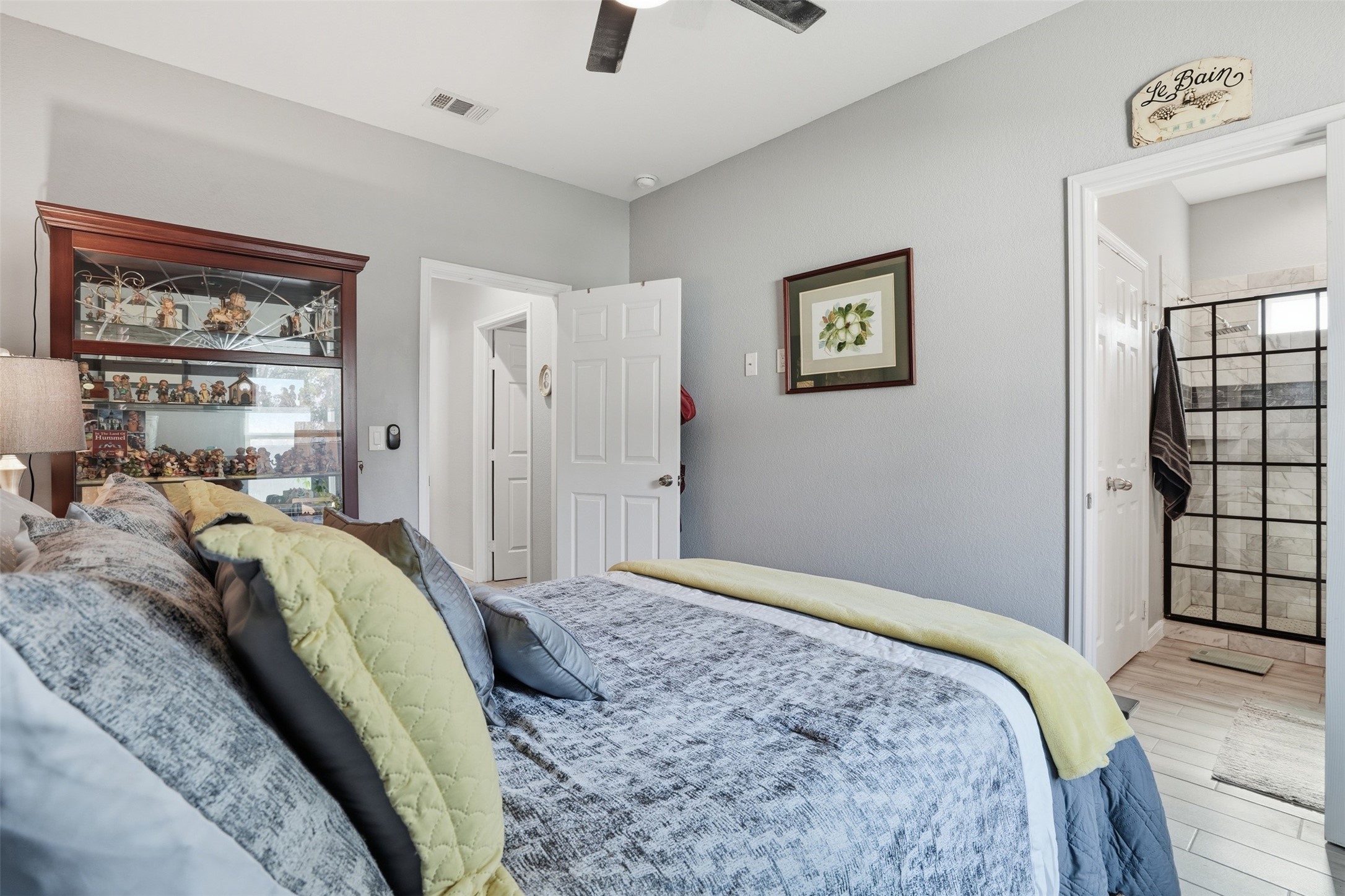 Cozy bedroom with elegant decor, featuring a comfortable bed with layered pillows and a stylish glass display cabinet. Adjacent is a sleek en-suite bathroom with modern fixtures.