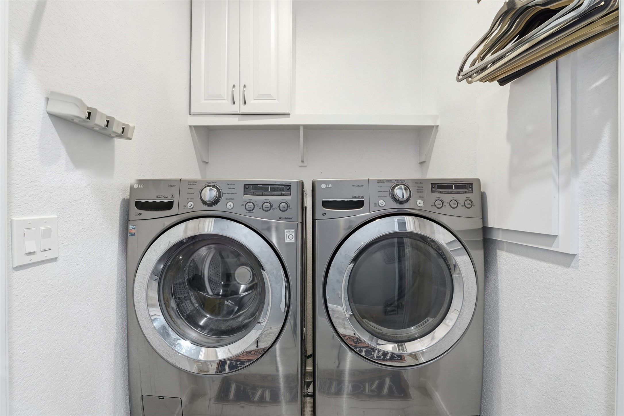 Laundry room with sleek stainless steel front-loading washer and dryer, ample shelving, and cabinet space for storage.