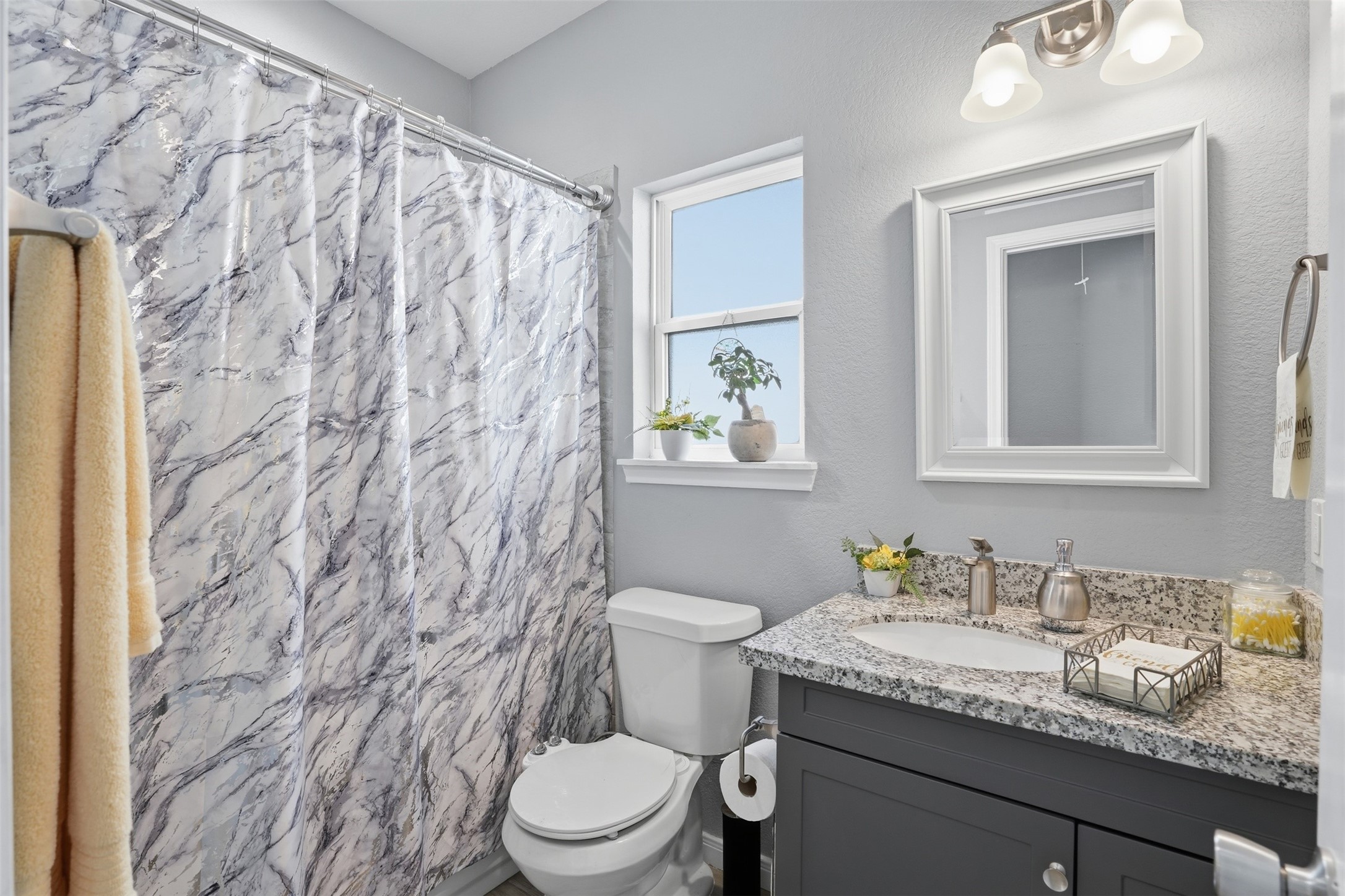 Bright and inviting bathroom featuring a marbled shower curtain, sleek granite countertop, and modern fixtures for a fresh, contemporary feel.
