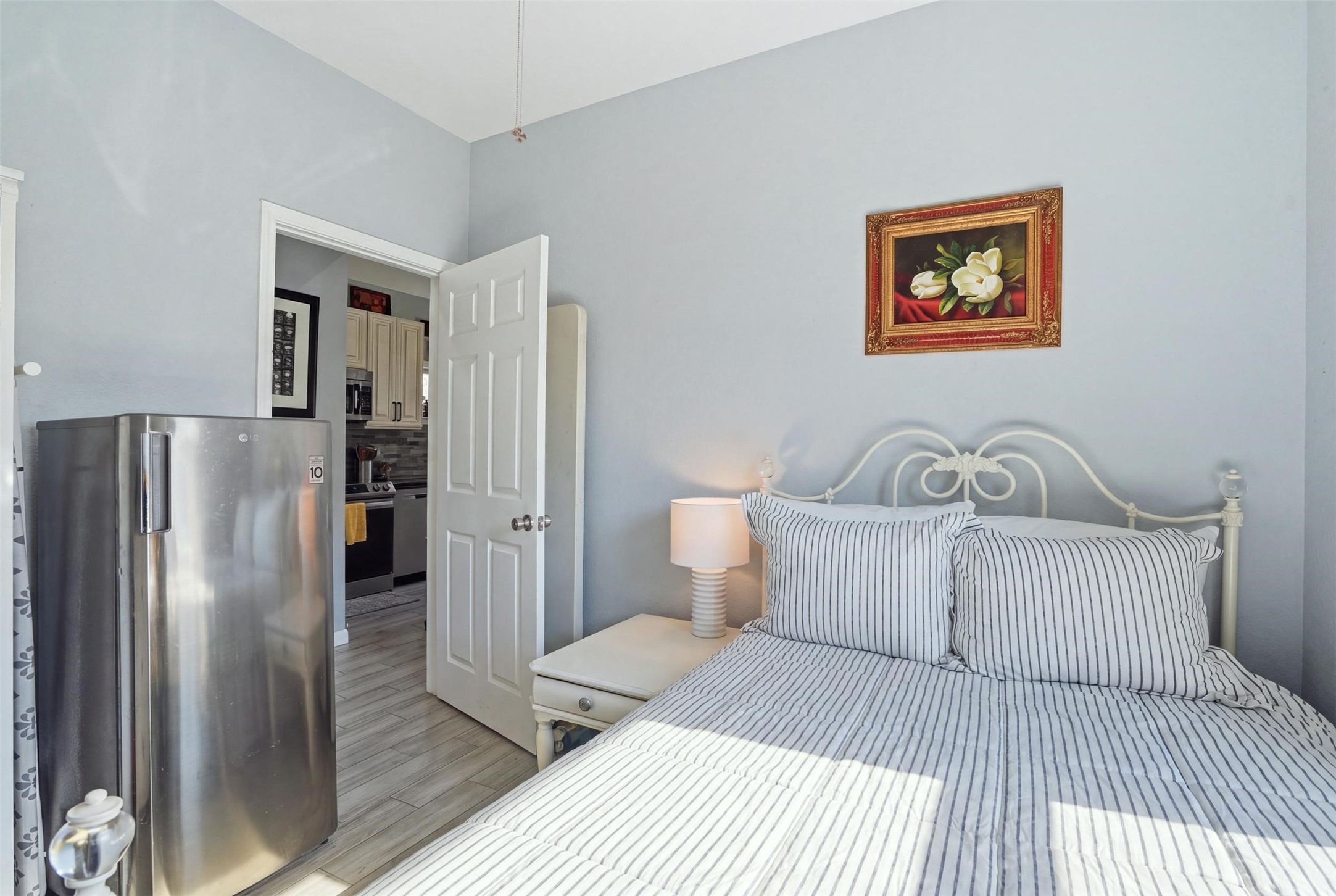 Bedroom with soft gray walls, featuring a stylish metal bed frame and striped bedding, complemented by a bedside lamp and decorative artwork.