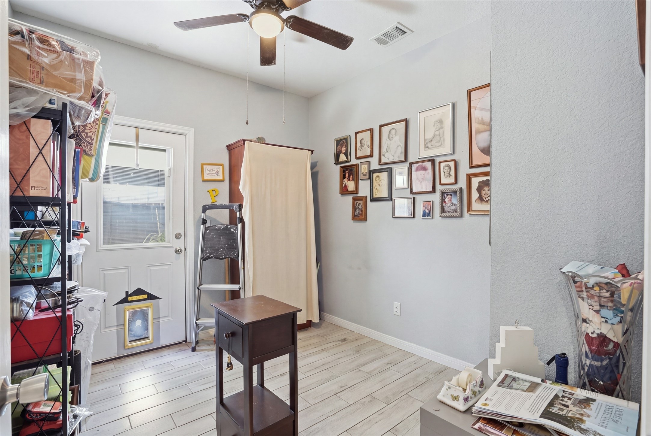 Bedroom with light wood flooring, wall-mounted artwork, and ample storage space, featuring a ceiling fan and natural light from the back door.
