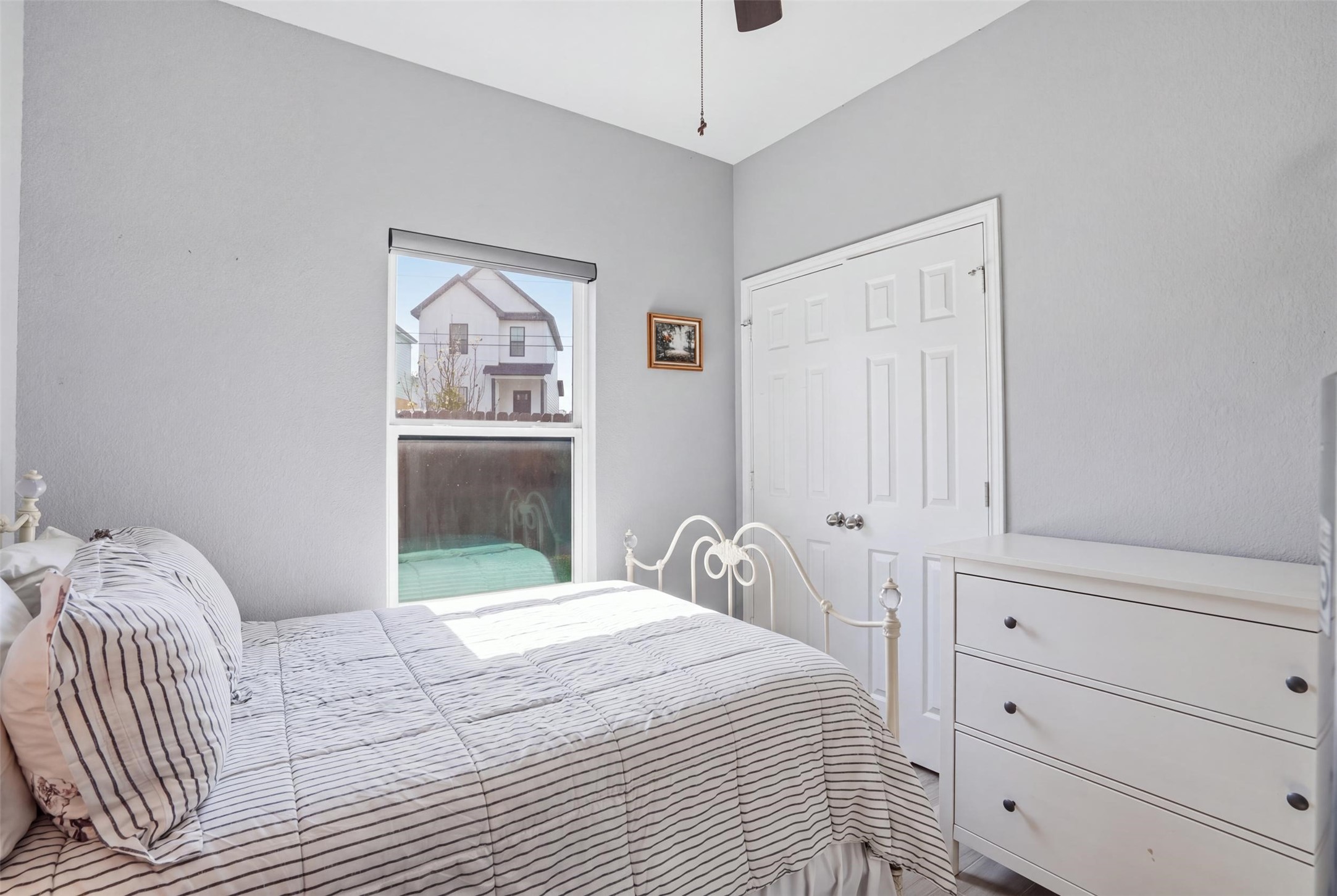 Bedroom featuring soft gray walls, ample natural light, and a classic white bed frame, complemented by a sleek white dresser.