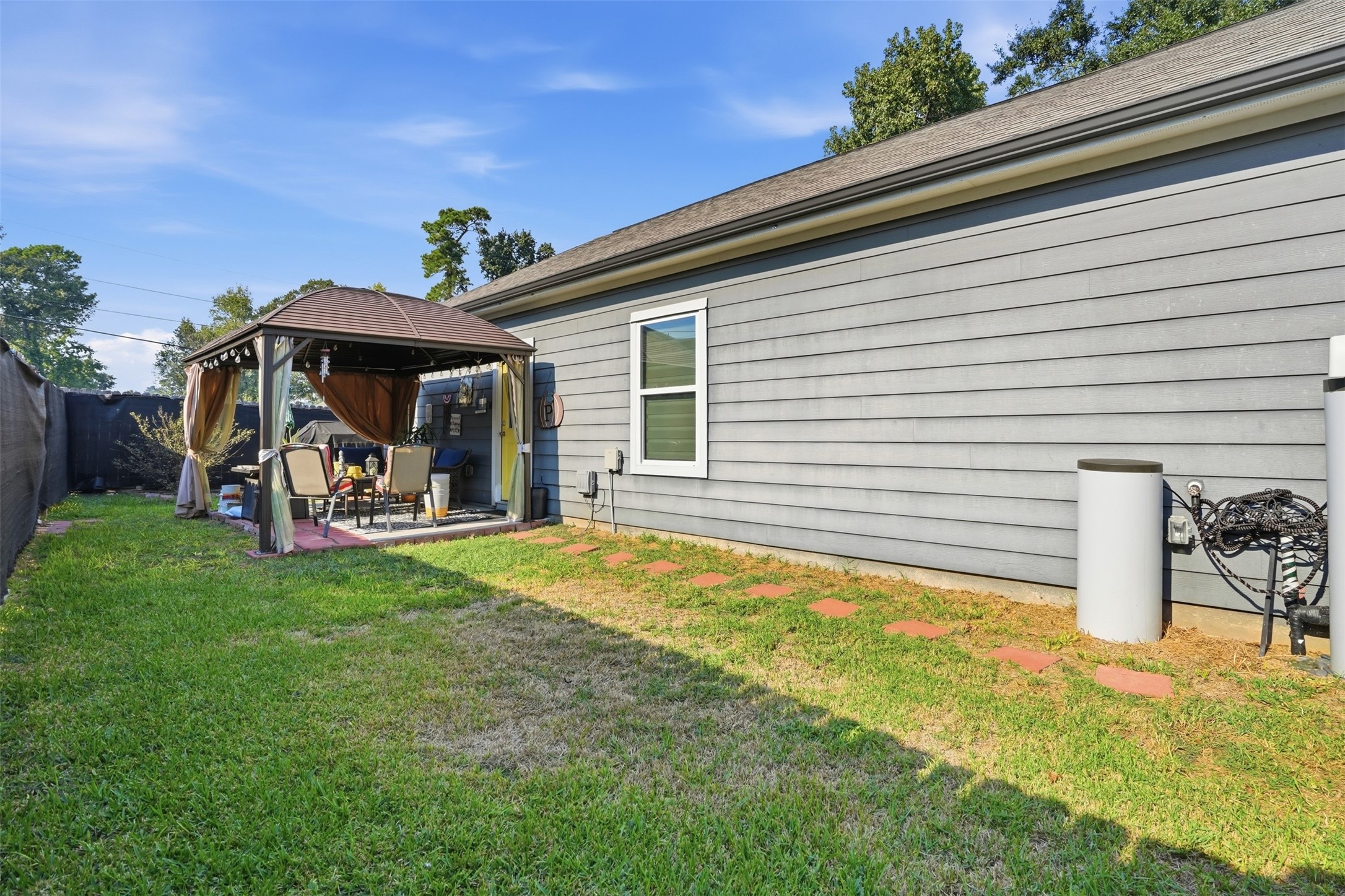 Charming backyard retreat features a cozy gazebo perfect for outdoor entertaining, surrounded by lush greenery and a well-maintained lawn.