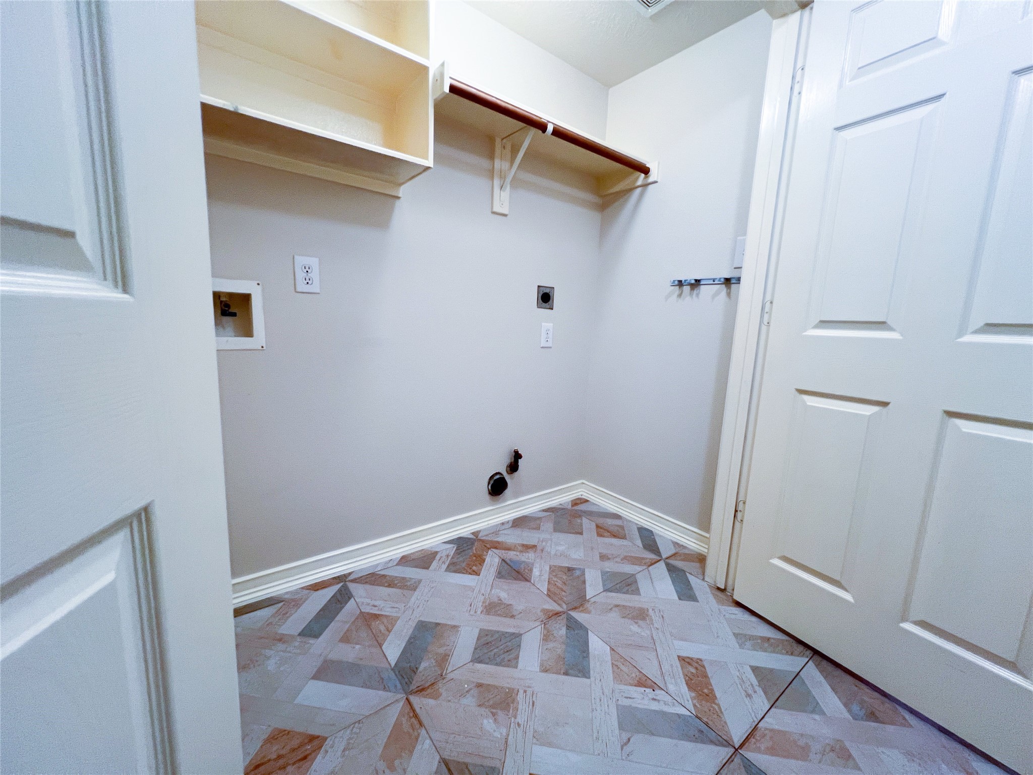 Spacious laundry room featuring ample shelving, convenient utility hookups, and stylish geometric tile flooring.