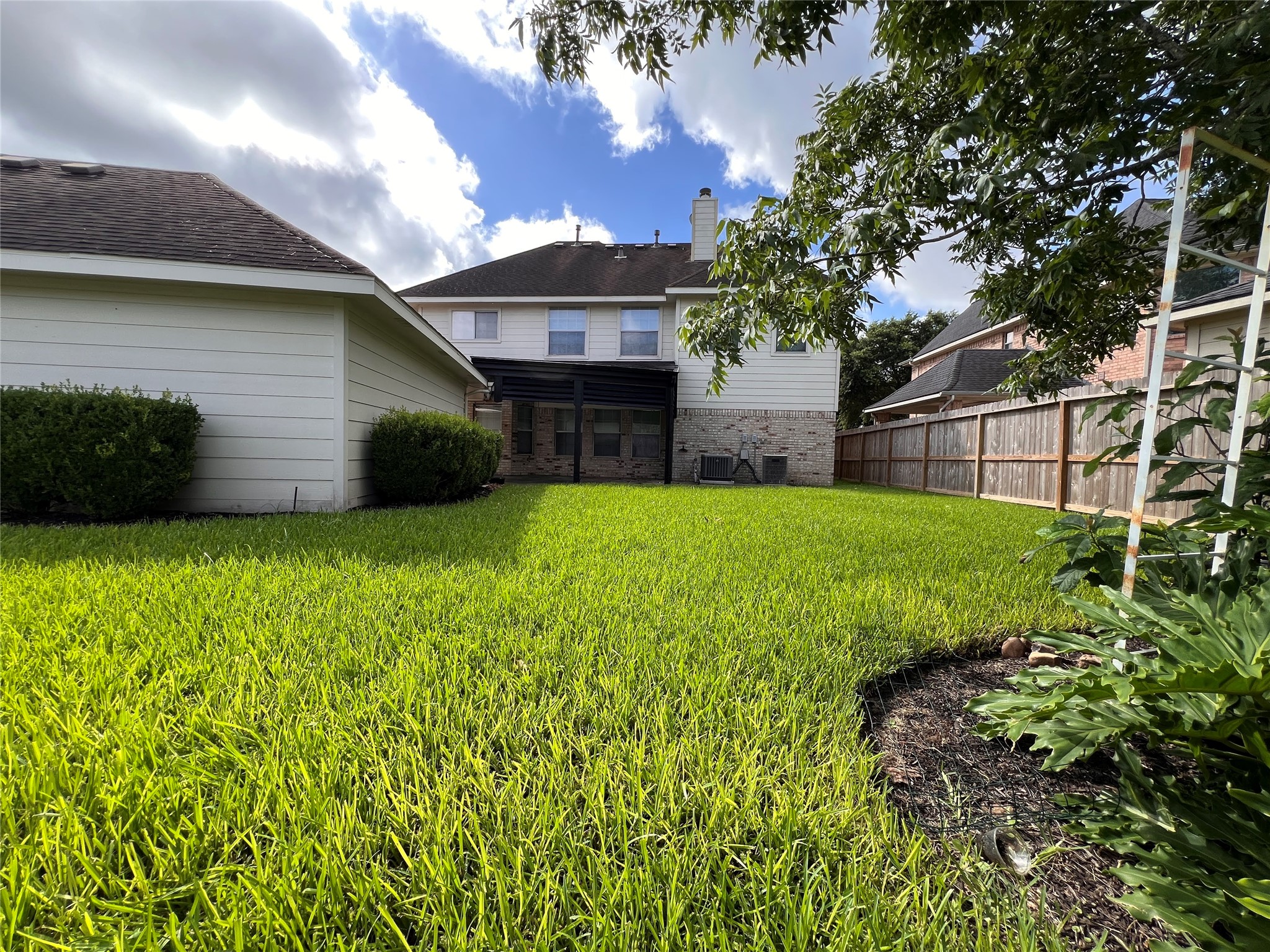 Spacious backyard with lush green lawn, mature trees, and a charming two-story home featuring a covered patio, perfect for outdoor relaxation.