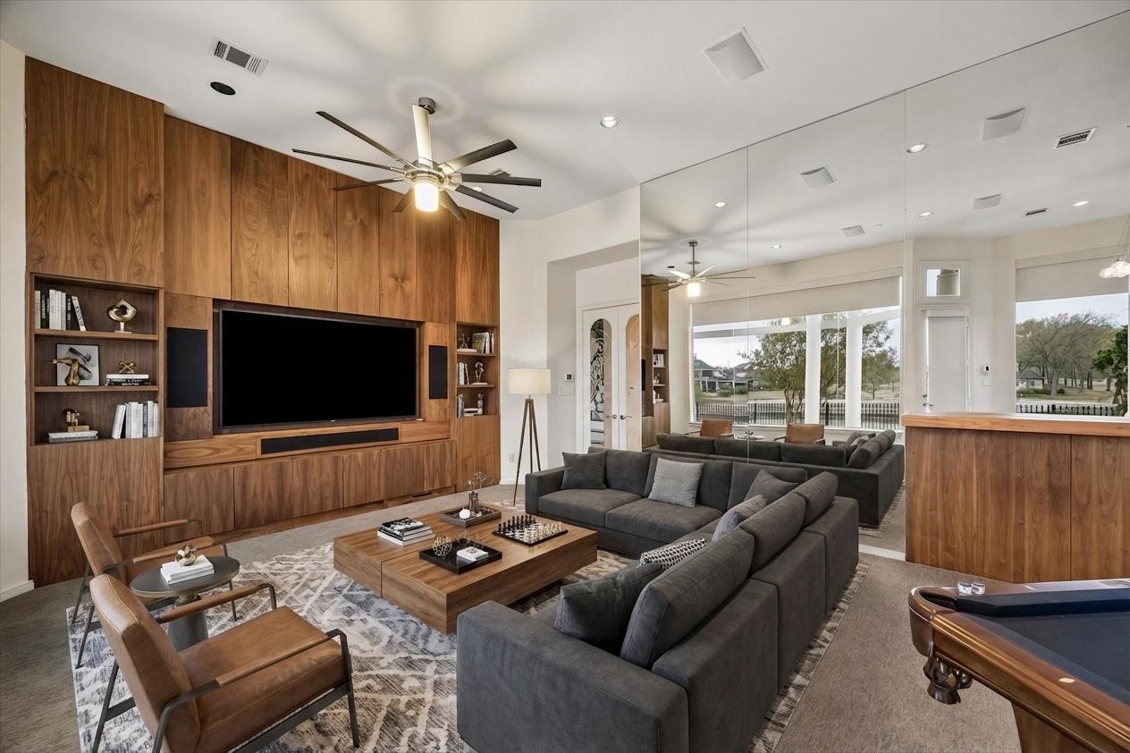 VIRTUALLY STAGED - media room/game room - wall of built-in cabinetry and large TV with built-in speakers, with pool table - enter though double doors with glass inserts, mirrored wall reflects the extensive outdoor terraces and lake view - door on exterior wall provides easy access to terraces, pool/spa and nearby outdoor kitchen