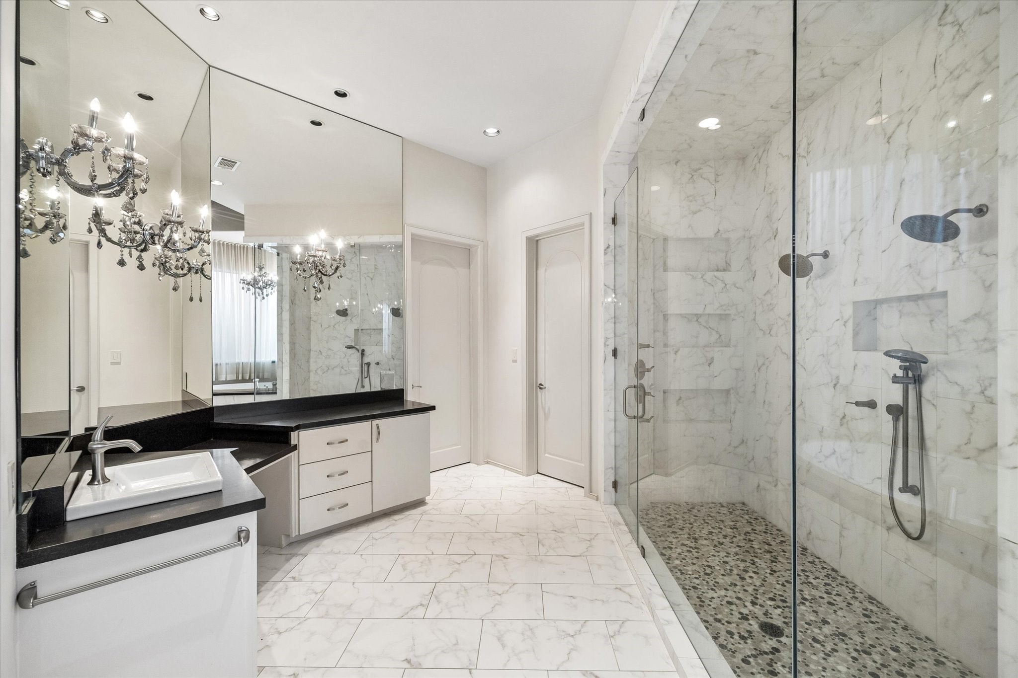 ANOTHER VIEW OF THE SPA-LIKE PRIMARY BATH RETREAT - a 2nd vanity area with built-in 'dressing table' space, large mirrors accented with sconces, door to right of vanity leads into the 2nd walk-in closet fitted with glazed-insert doors protecting clothing with hanging space and storage