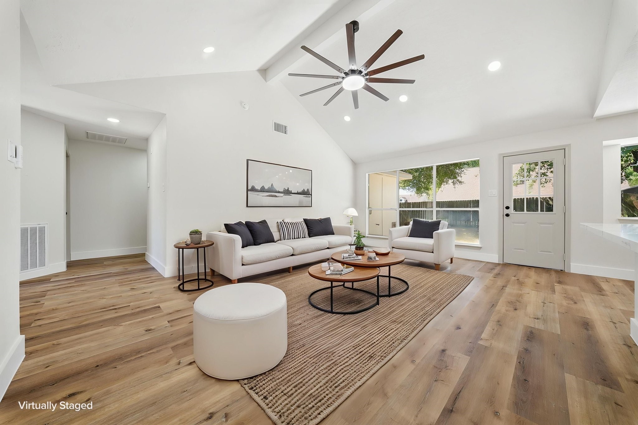 Bright and spacious living area featuring vaulted ceilings, a modern ceiling fan, and warm LVN flooring, seamlessly connecting to a large window and glass door for abundant natural light.