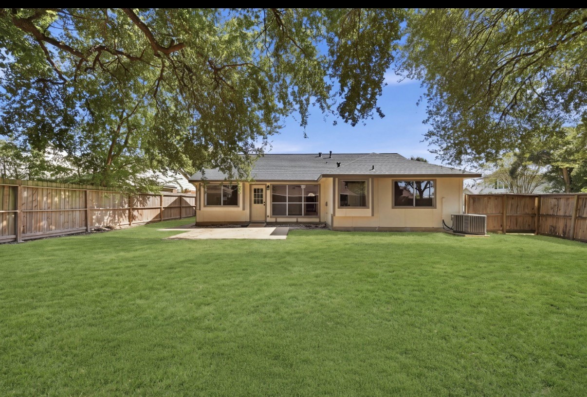 Charming backyard with lush green grass, a spacious patio for outdoor entertaining, and mature trees providing ample shade, all enclosed by  wooden fence for privacy.