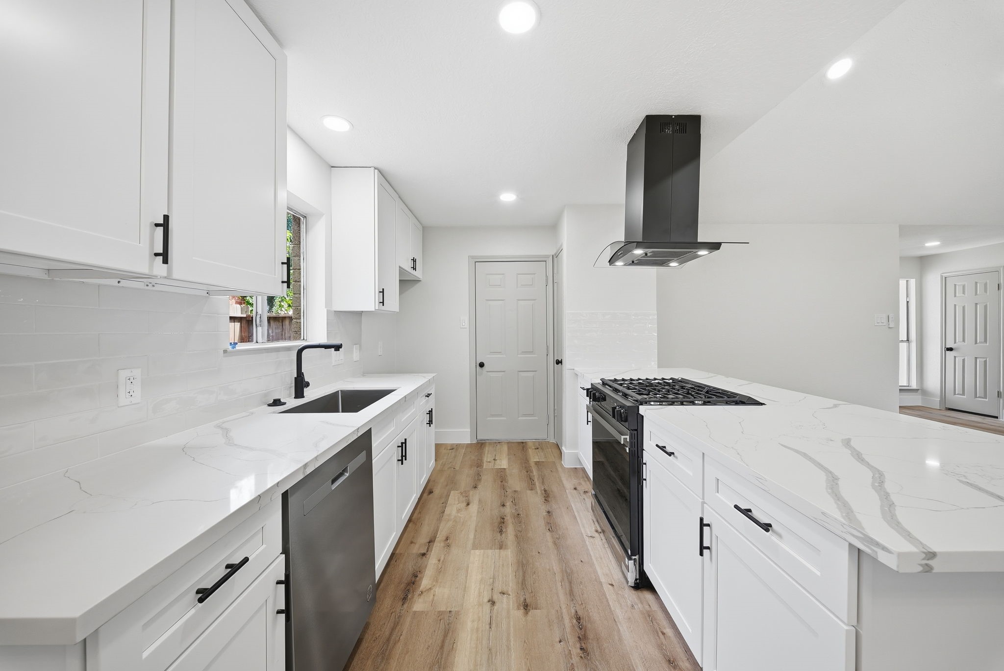 The kitchen features modern appliances, sleek white cabinetry, and elegant quartz countertops. Large windows above the sink invite the beauty of the outdoors inside.