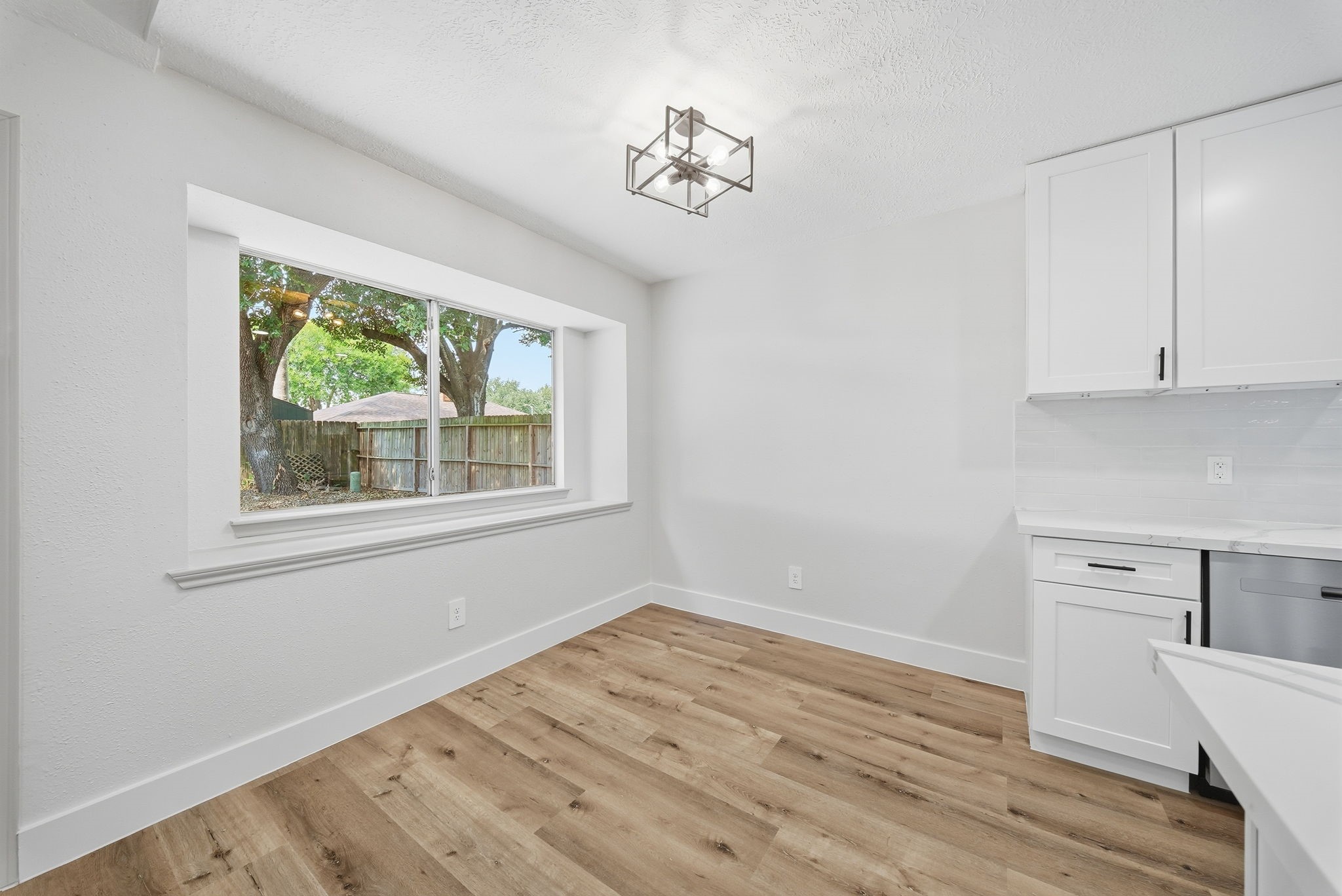 Bright and inviting kitchen area featuring a large bay window, modern light fixture, and sleek white cabinetry, complemented by warm LVN flooring.
