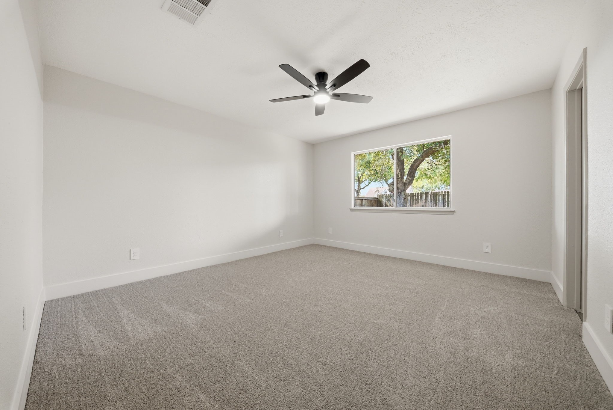 Spacious bedroom with plush carpeting, a large window offering natural light, and a modern ceiling fan for comfort.
