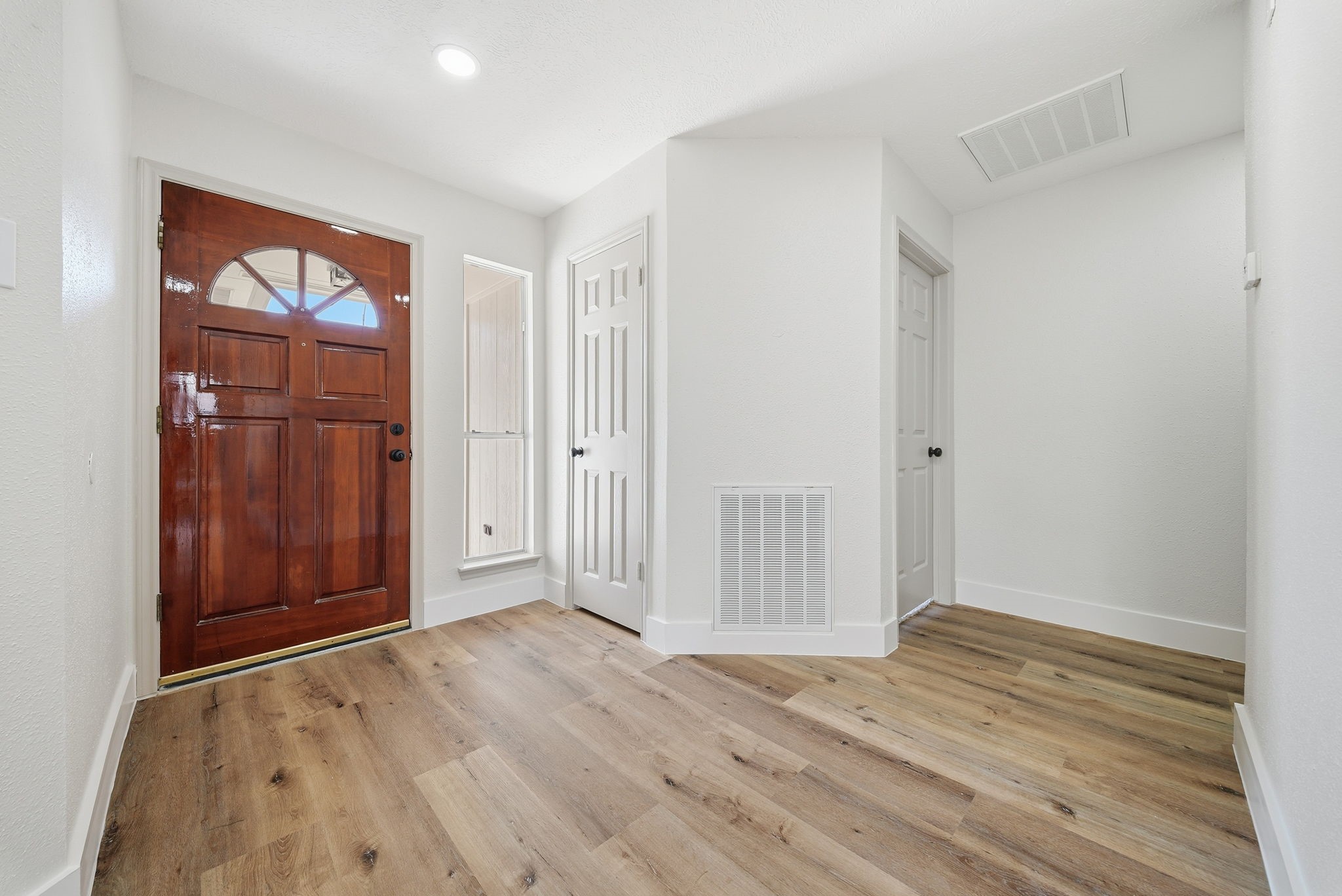 The entryway showcases a wood arch window front door, complemented by light-color walls and LVP flooring.