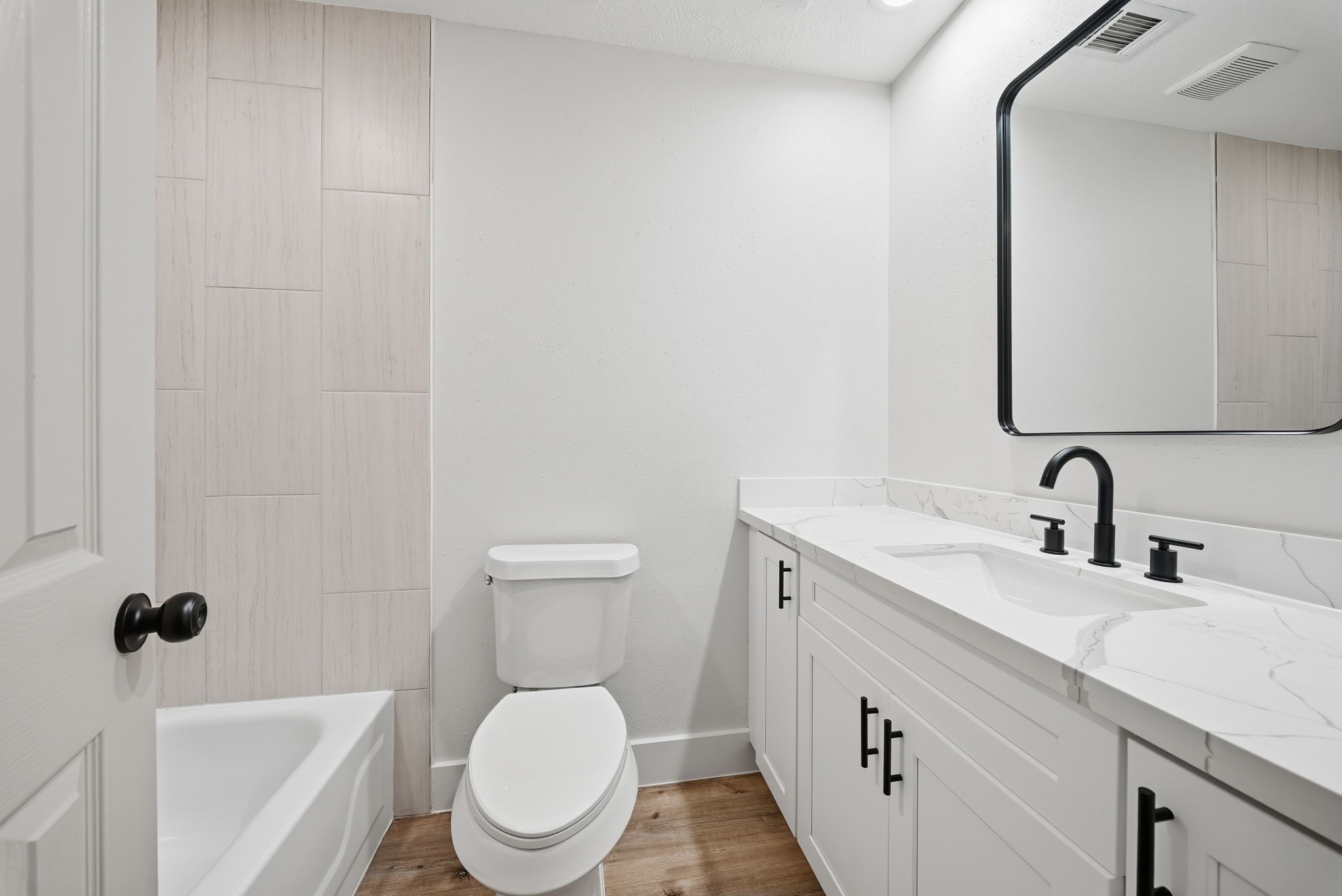 Modern bathroom featuring a sleek double vanity with elegant black fixtures, a spacious mirror, and a pristine bathtub surrounded by light tile accents.