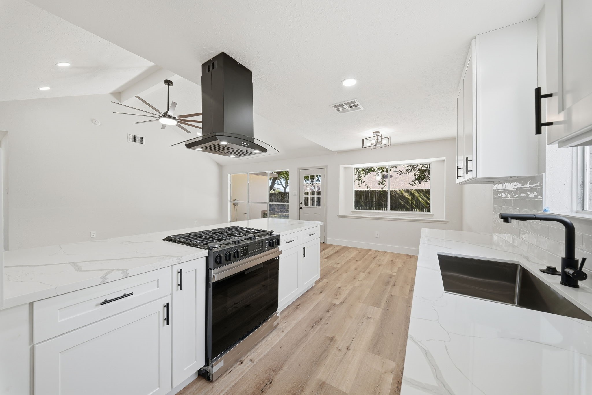 Sleek kitchen with modern gas burner stove with range appliances, seamlessly opening into a bright living area with large windows and stylish light fixtures.
