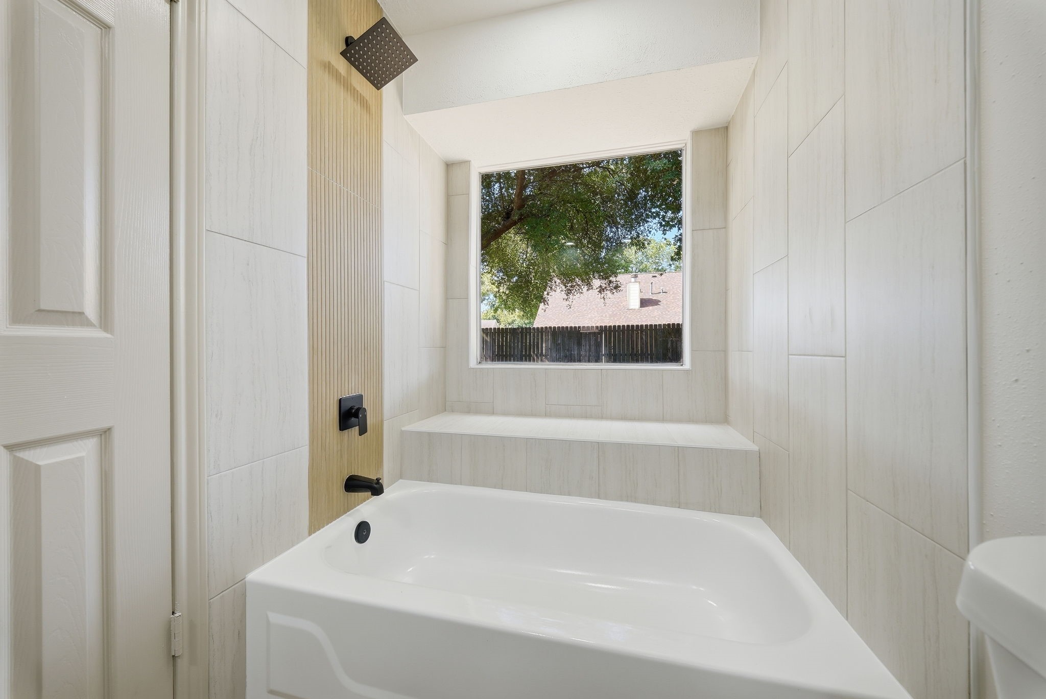 Inviting bathroom featuring a modern soaking tub and a large window and seat, providing natural light and a serene view.