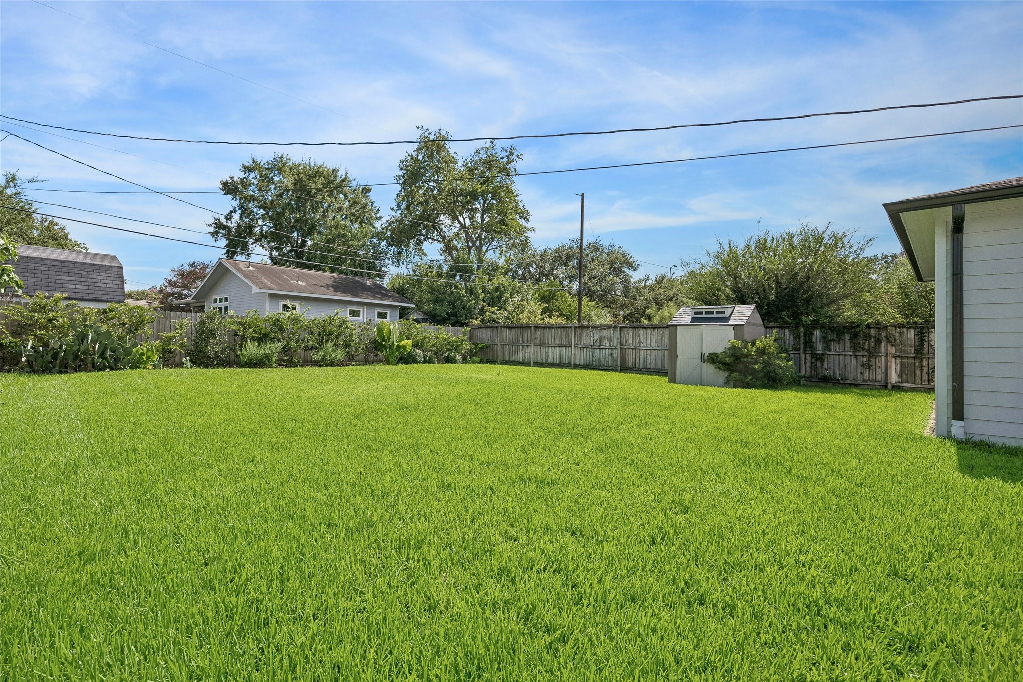Expansive backyard with lush green grass, perfect for outdoor activities, bordered by a wooden fence and featuring a convenient storage shed.