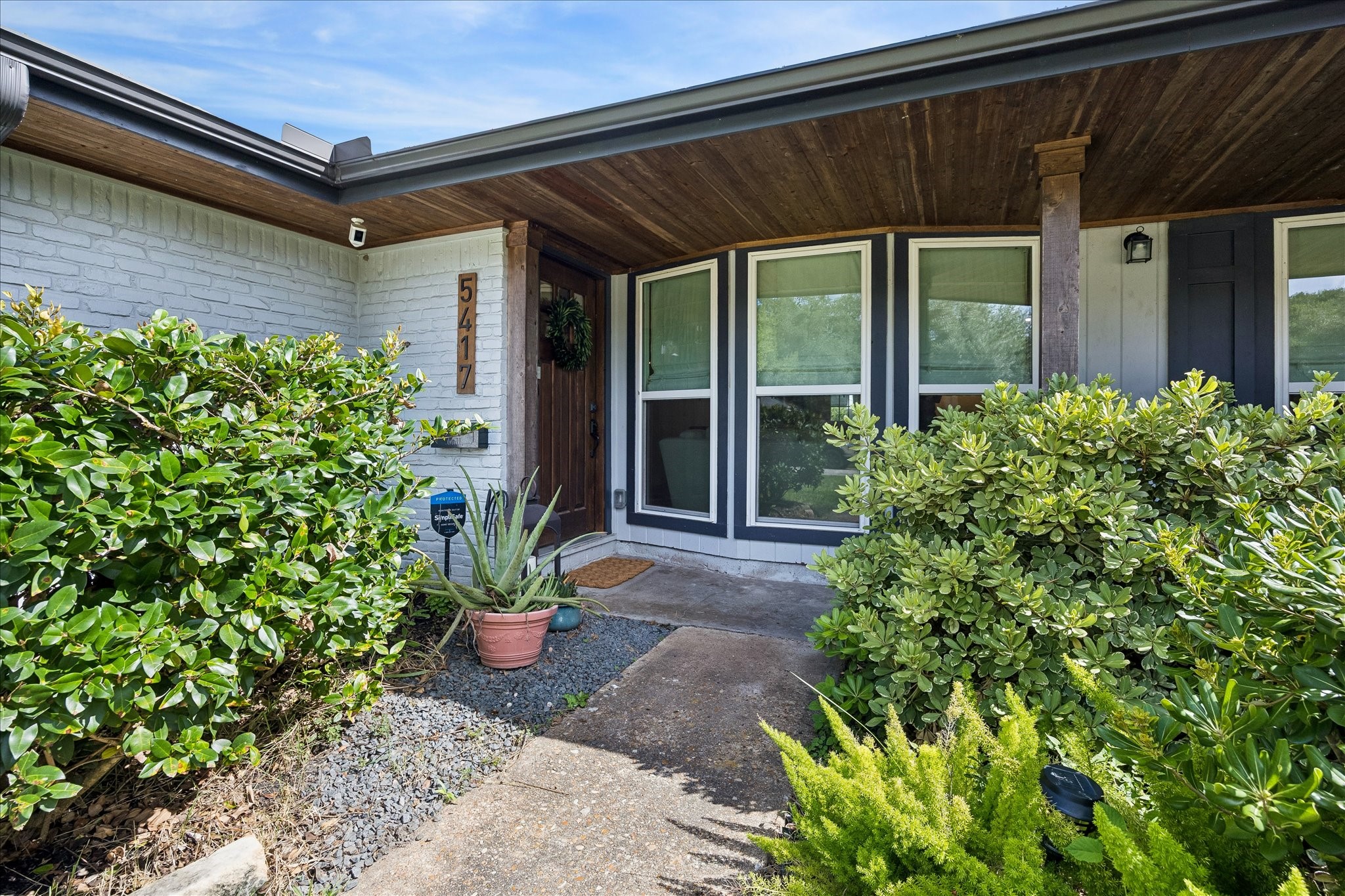 Charming entrance with a covered porch and lush greenery, offering a welcoming approach to the home.