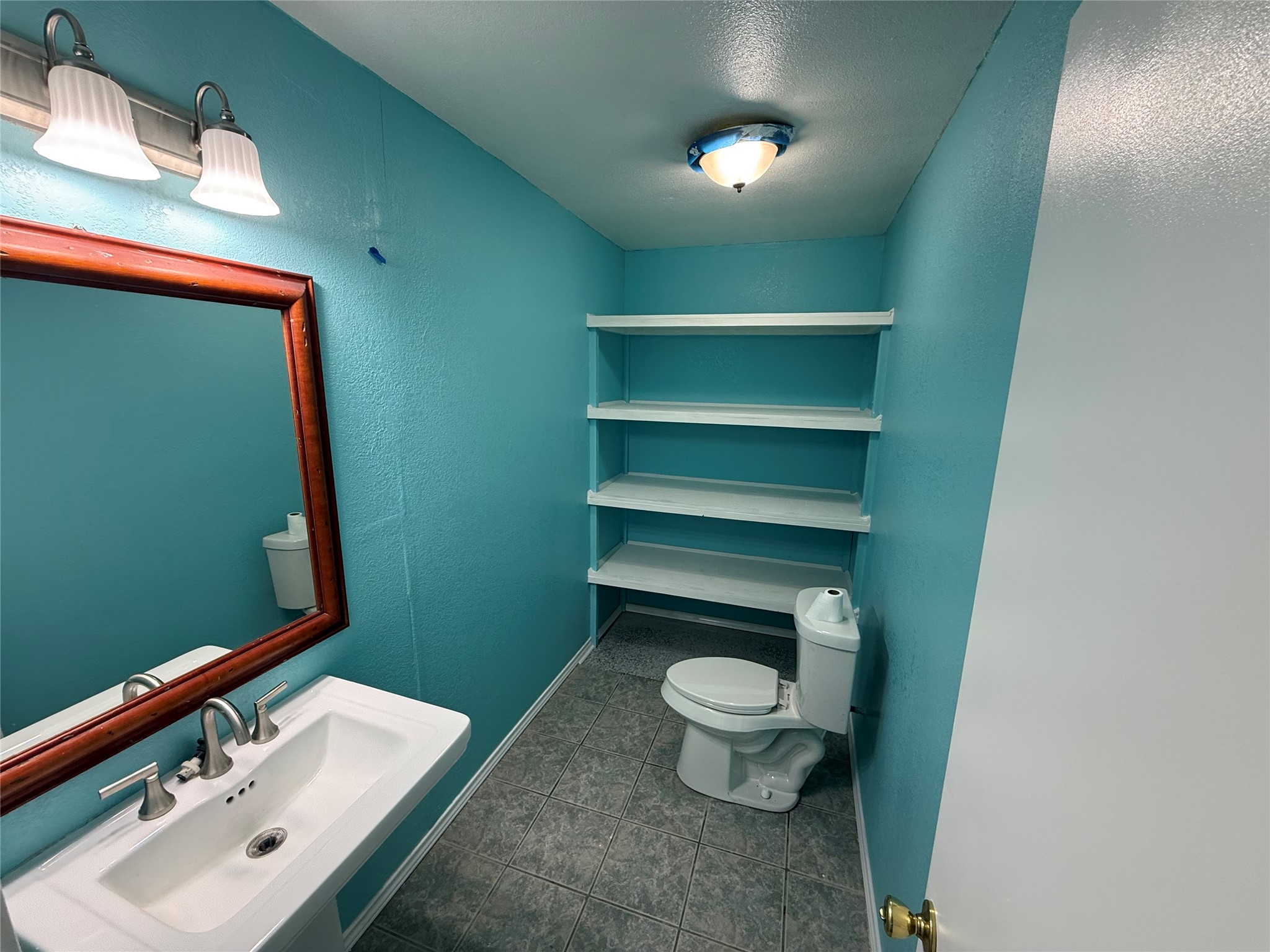 Bathroom with a framed mirror, vanity, and open shelving above the toilet.