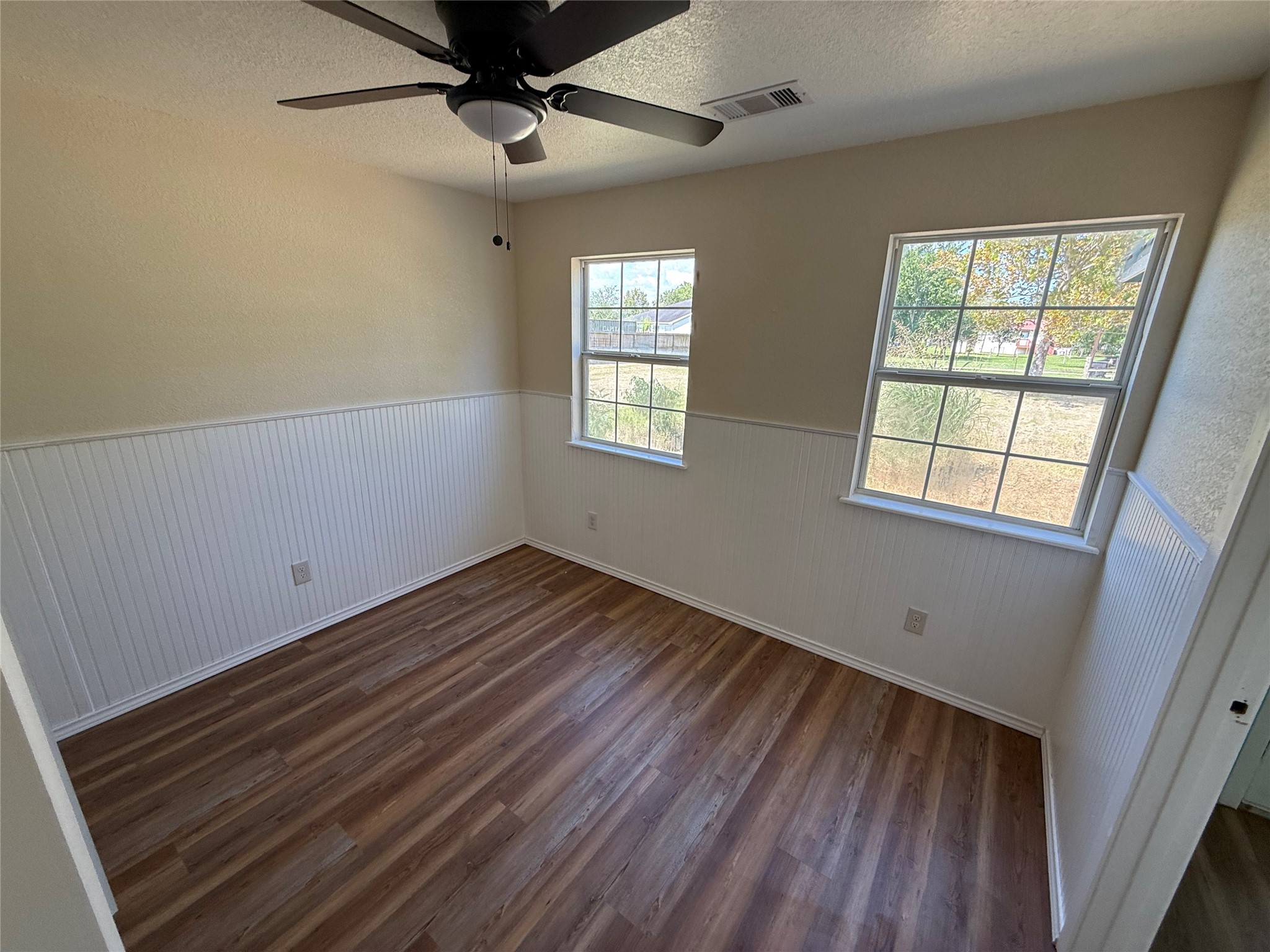 Corner room with multiple windows, wood-look flooring, and a ceiling fan.