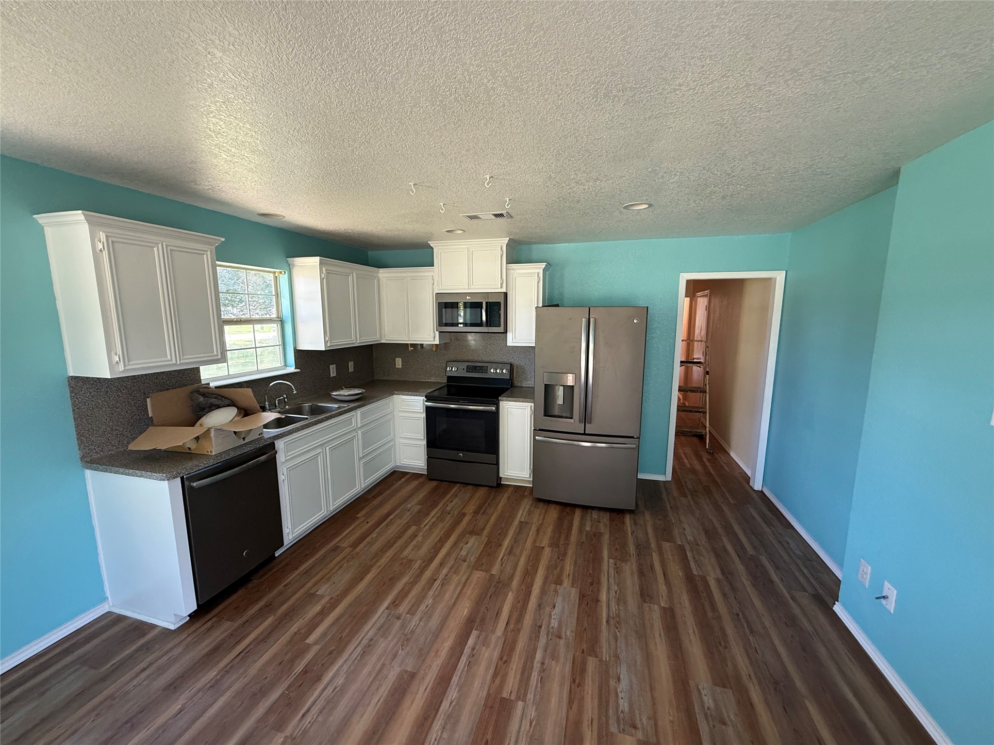 Spacious kitchen with white cabinetry, stainless steel appliances, and wood-look flooring.