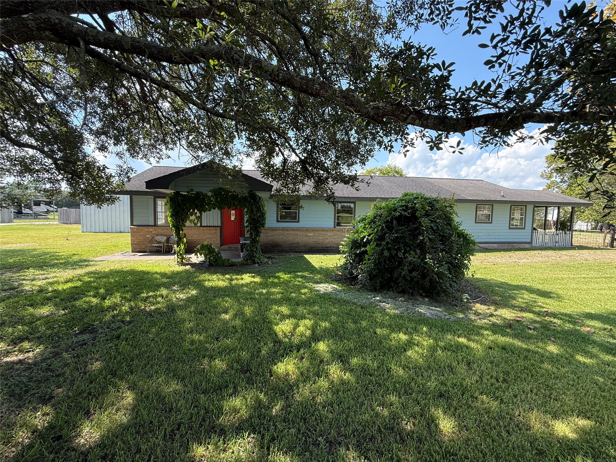 Front exterior with mature shade trees, a covered entry, and a spacious lawn.