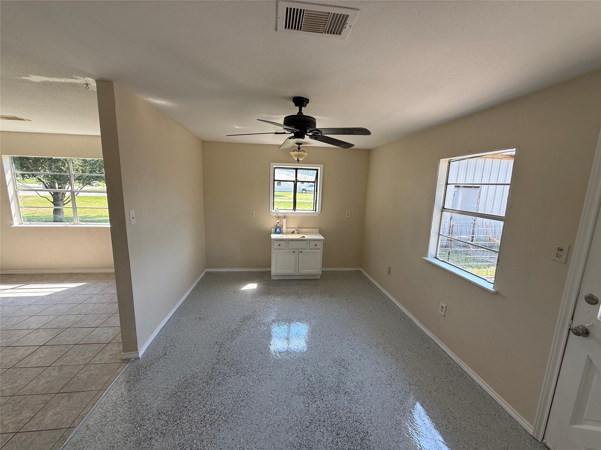 Bright gathering space with tile flooring, multiple windows, and a ceiling fan.