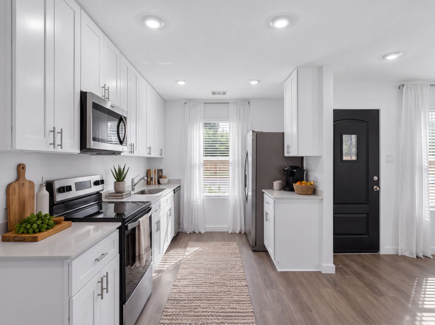 Kitchen with white cabinets, stainless steel appliances, and a coffee-bar counter near the rear entry door. Recessed lighting and a window fill the galley layout with light.
This photo has been digitally staged to illustrate the possibilities of the home's aesthetic and potential design. Some furnishings and dcor shown are for visual inspiration.