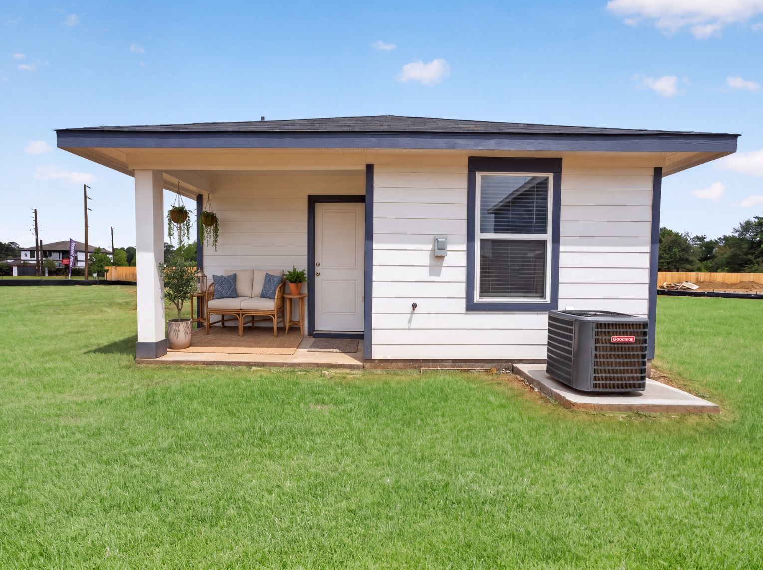 Rear exterior showing the covered porch, lap siding with navy trim, and a large open lawn. The Goodman AC unit sits on a concrete pad alongside the home.
This photo has been digitally staged to illustrate the possibilities of the home's aesthetic and potential design. Some furnishings and dcor shown are for visual inspiration.