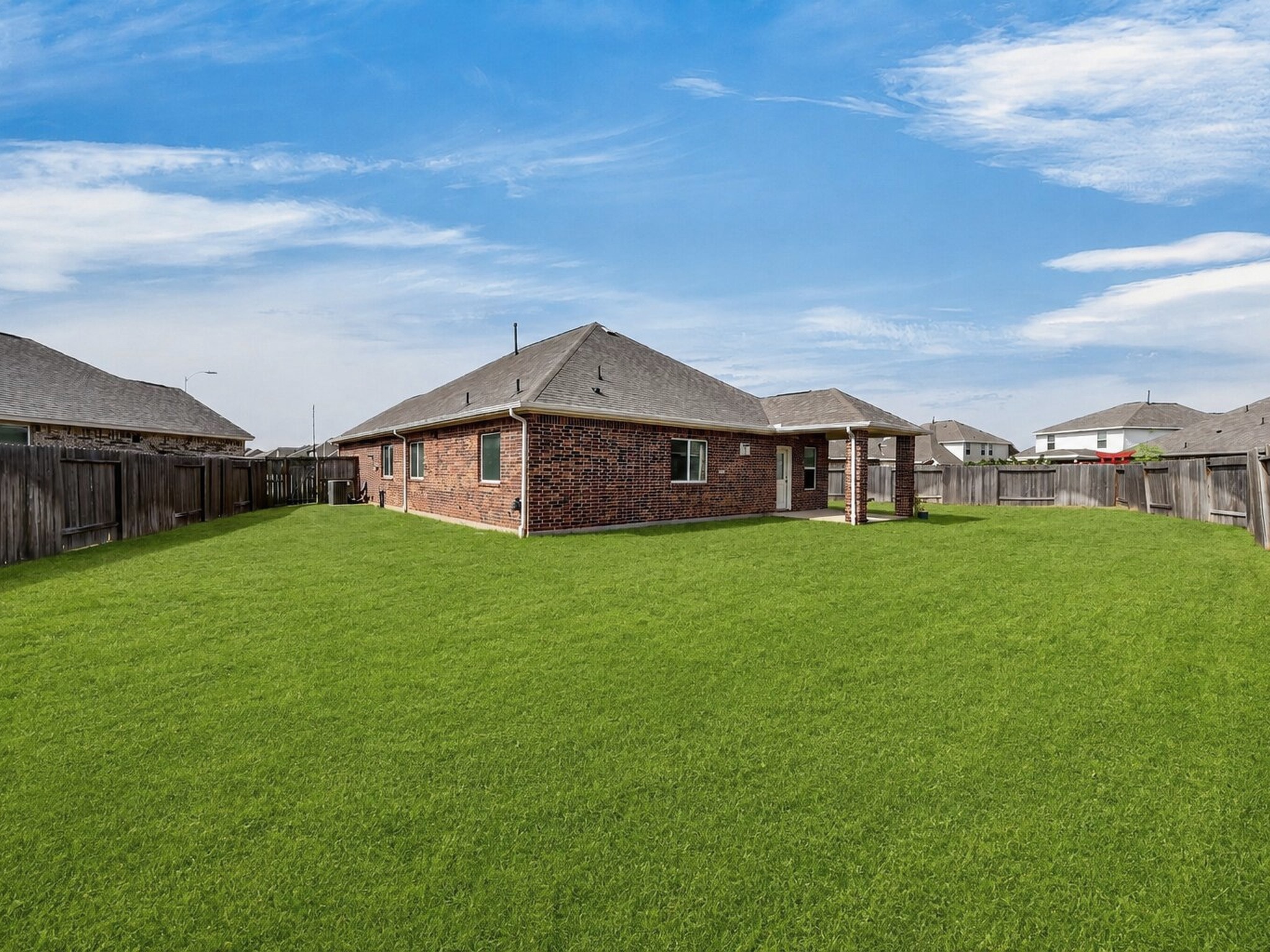 Rear exterior view showcases the expansive lawn, covered patio, and fenced backyard.