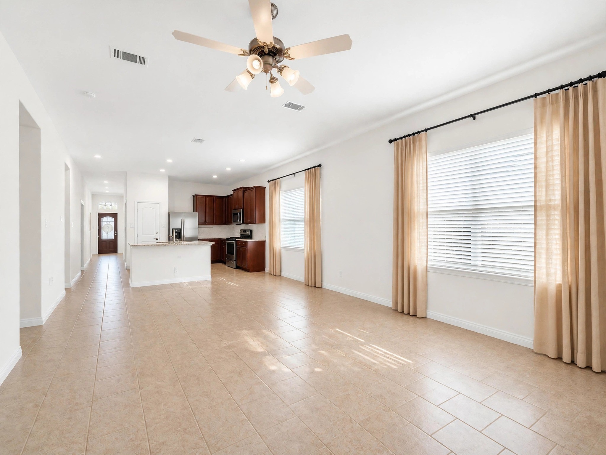 Unfurnished view of the living area highlights the tile flooring, large windows, and open kitchen connection. Unfurnished view of the living area highlights the tile flooring, large windows, and open kitchen connection.