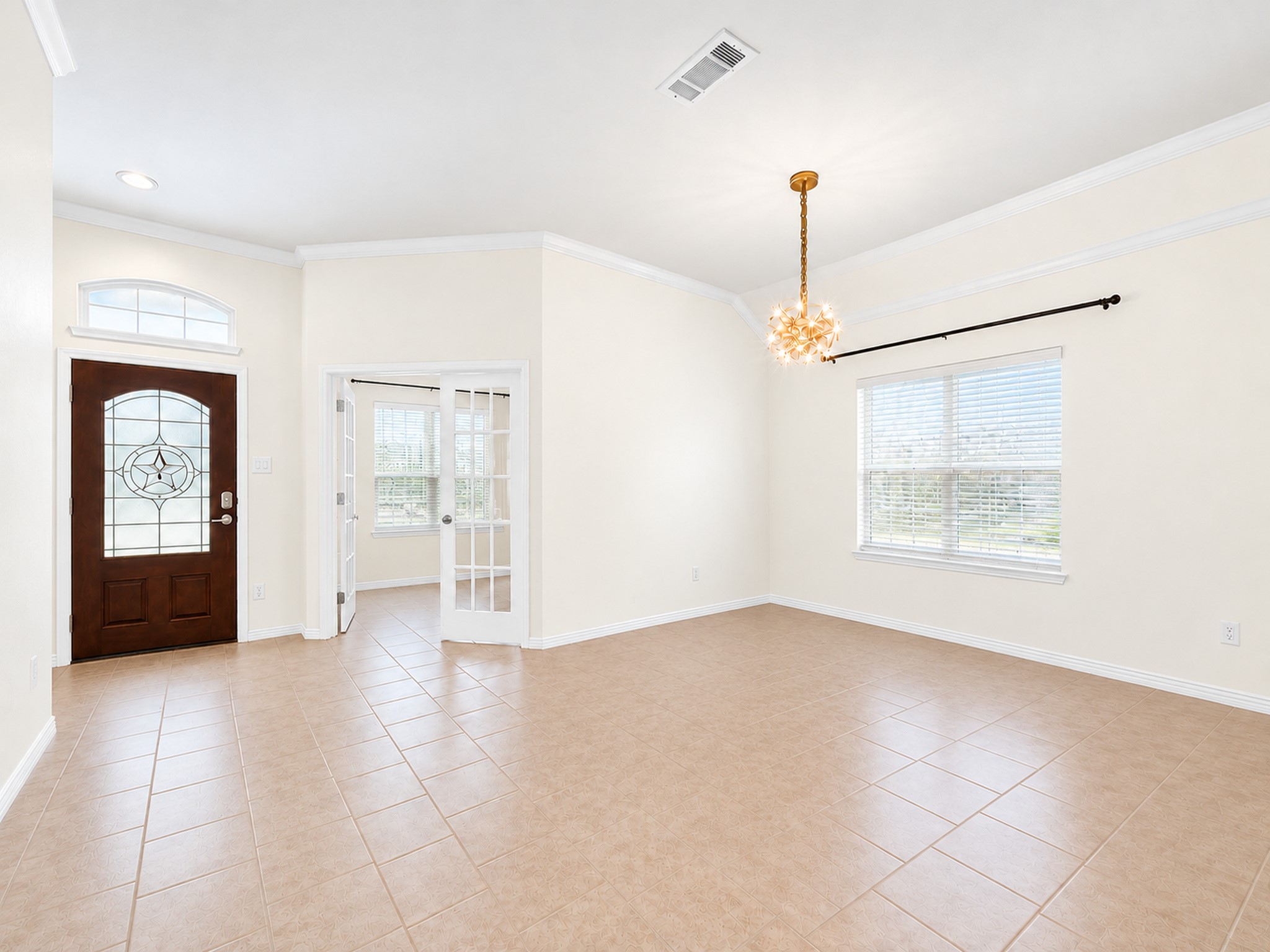 Furniture and personal dcor have been digitally removed to showcase the dining rooms layout, tile flooring, crown molding, and natural light. French doors connect to an adjacent room near the front entry. Furniture and personal dcor have been digitally removed to showcase the dining rooms layout, tile flooring, crown molding, and natural light. French doors connect to an adjacent room near the front entry.