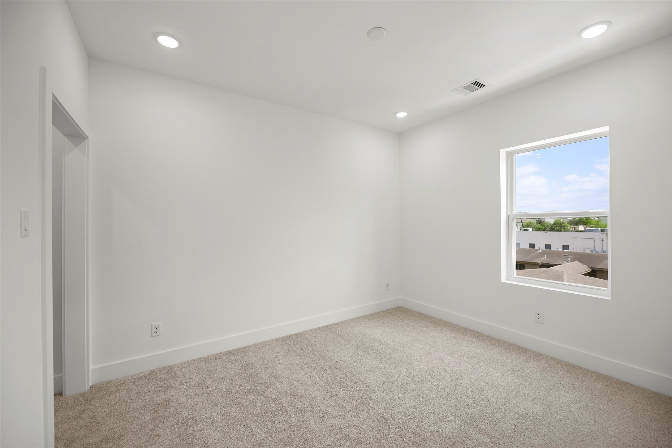 This secondary bedroom on the third level is bright, carpeted, white walls, recessed lighting, and a window offering natural light and an outdoor view.