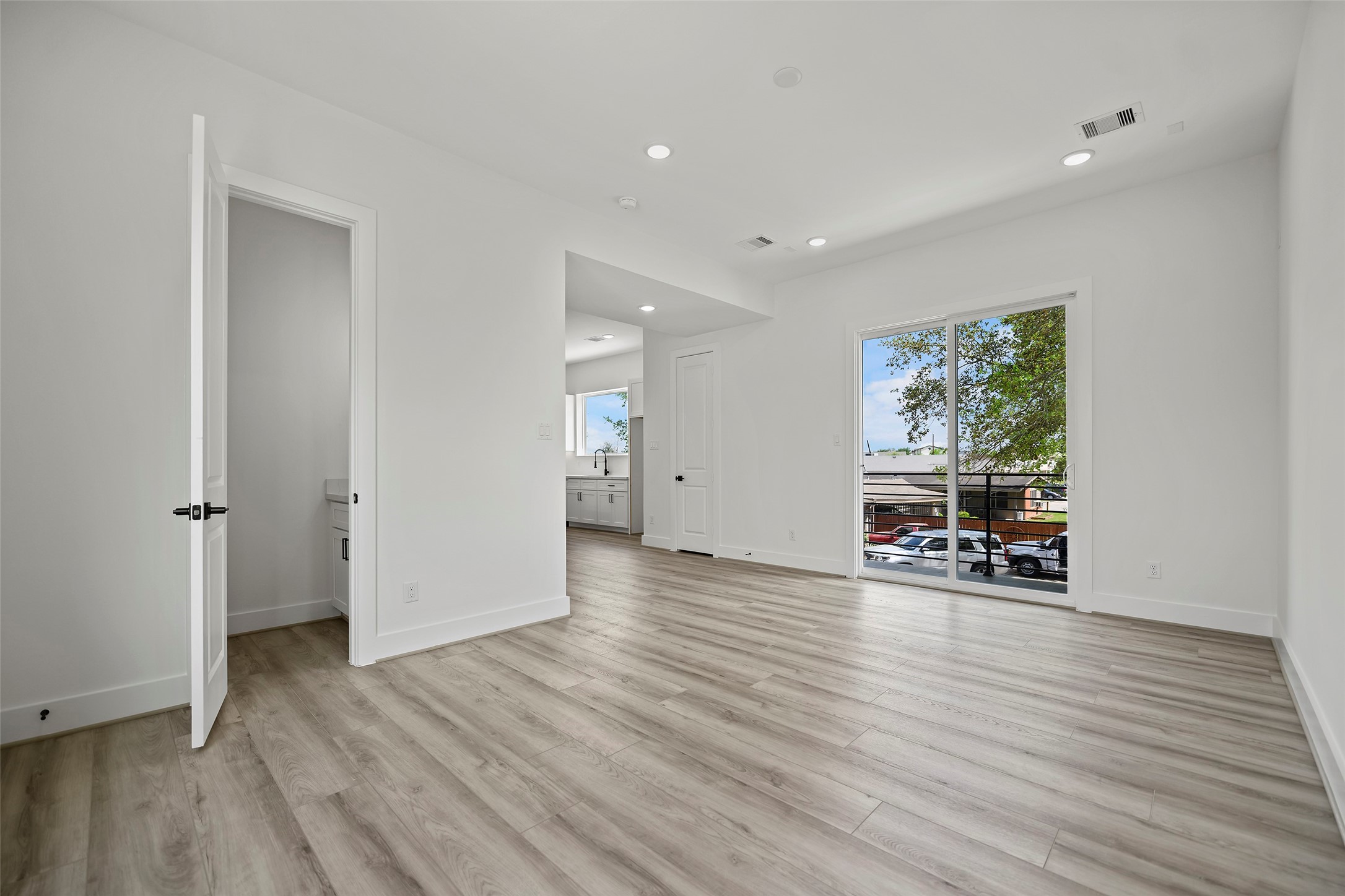 The living area showcases a bright and spacious room with modern LVP flooring, recessed lighting, and natural walls.  It features an open layout with a staircase leading down, ideal for versatile use and customization.