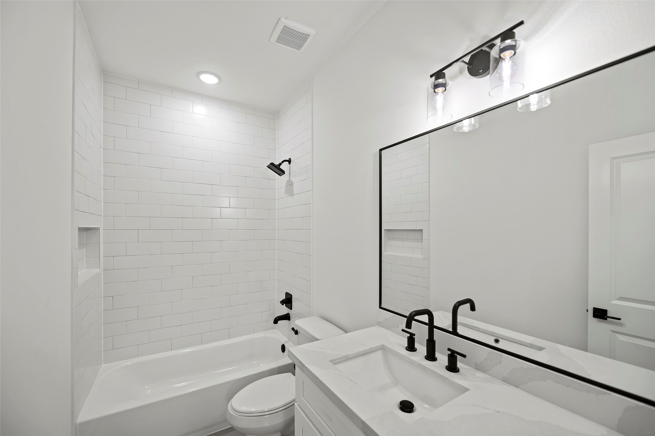 This first level bathroom features a sleek, modern design with white subway tile walls, a built-in bathtub, and a stylish vanity with a large mirror.  Black fixtures add a contemporary touch.
