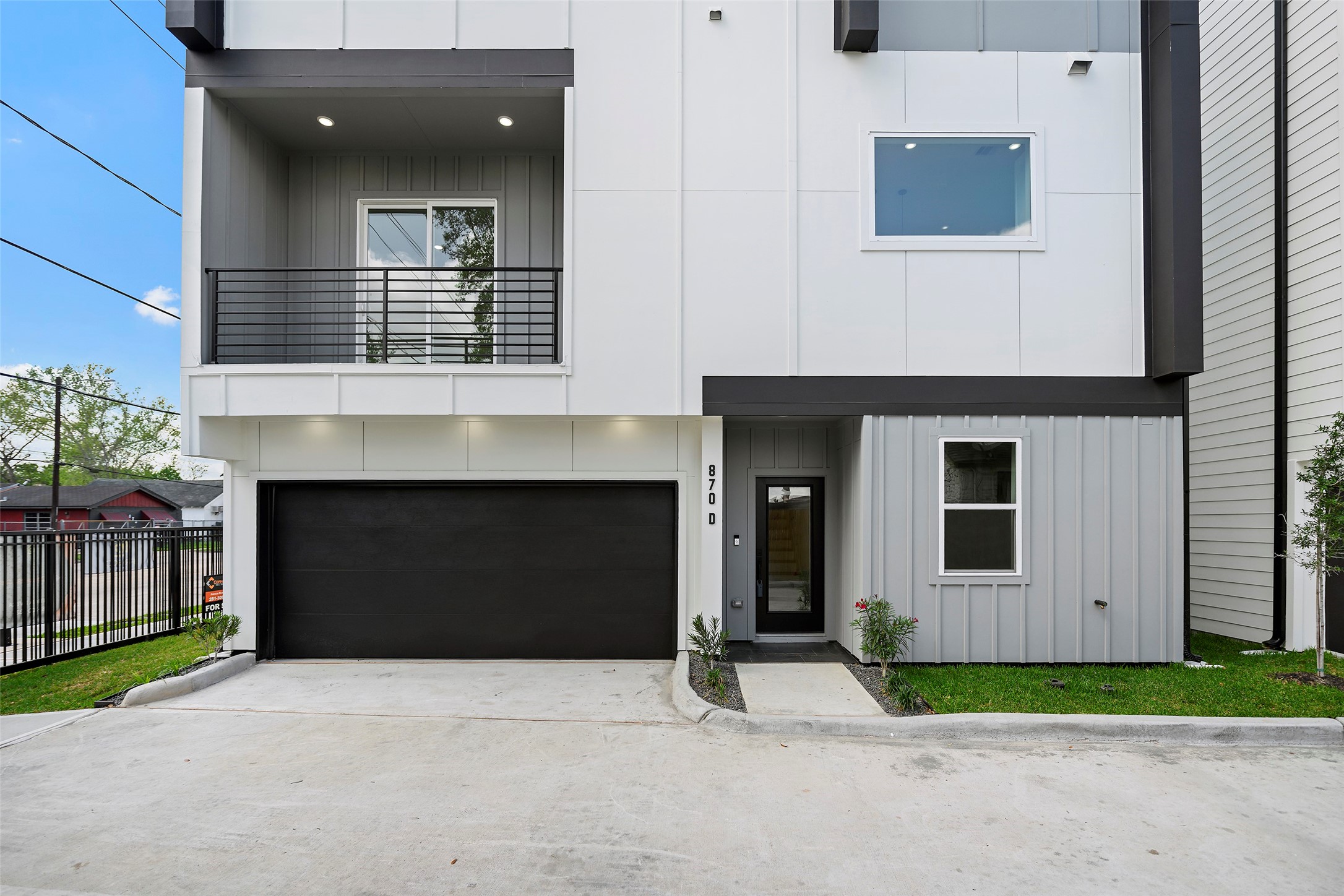 Modern three-story townhouse with a  sleek facade, featuring a two-car garage and a small balcony.  The entrance is framed by clean lines and minimalistic landscaping, offering a contemporary urban living vibe.