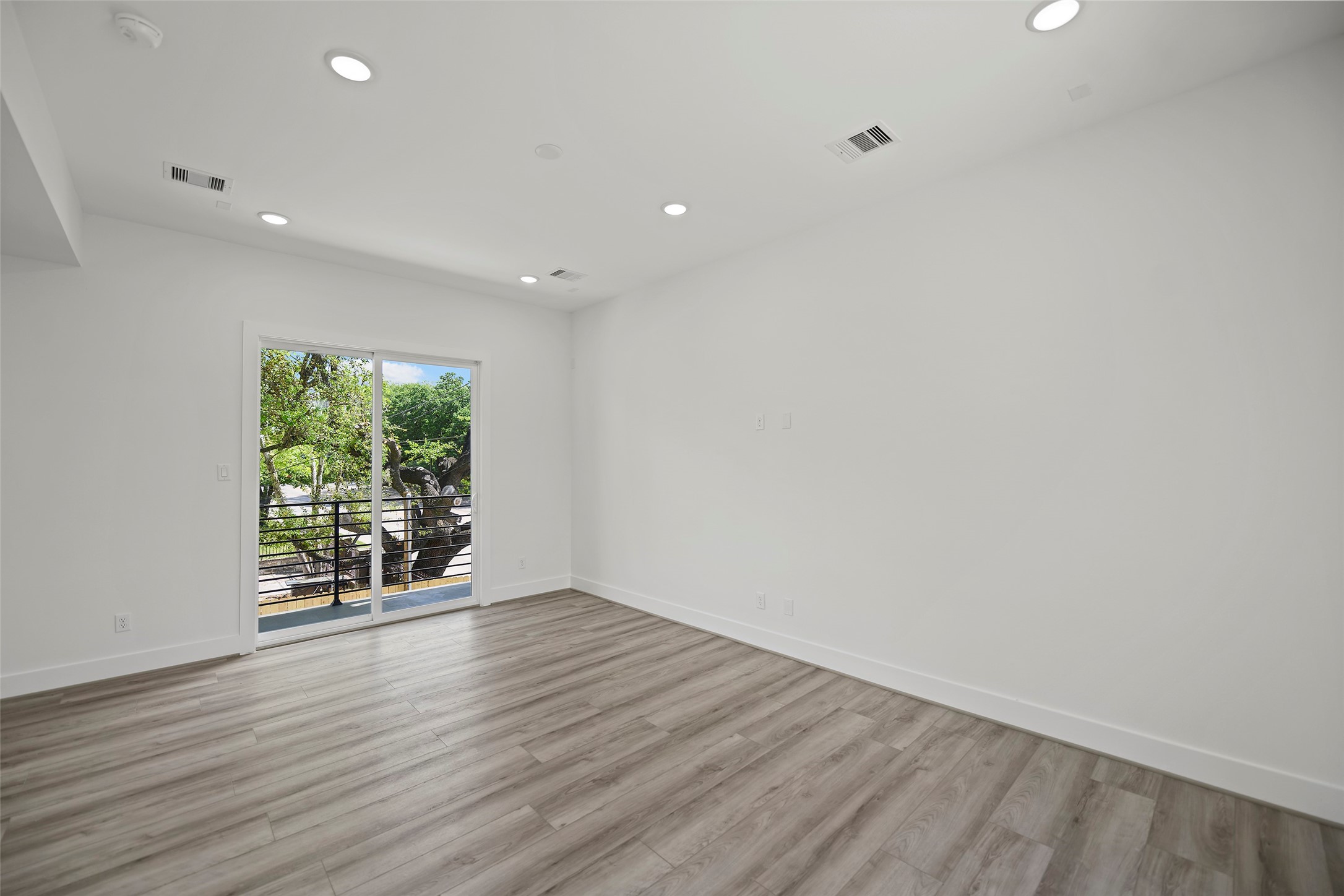 The living area features modern LVP flooring, recessed lighting, and a large sliding glass door leading to a balcony with a view of lush greenery, creating a bright and inviting space.