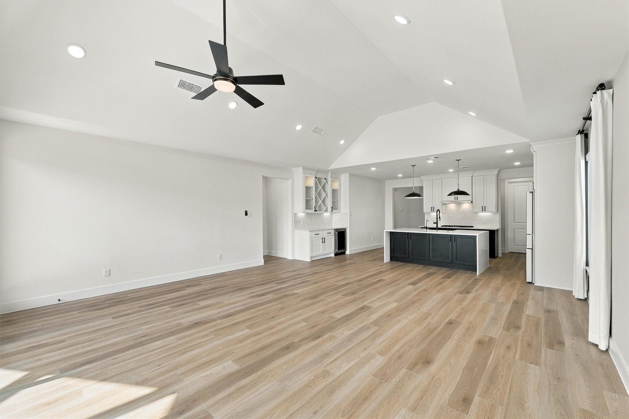 The open-concept great room flows into the kitchen and dry bar under a dramatic vaulted ceiling.