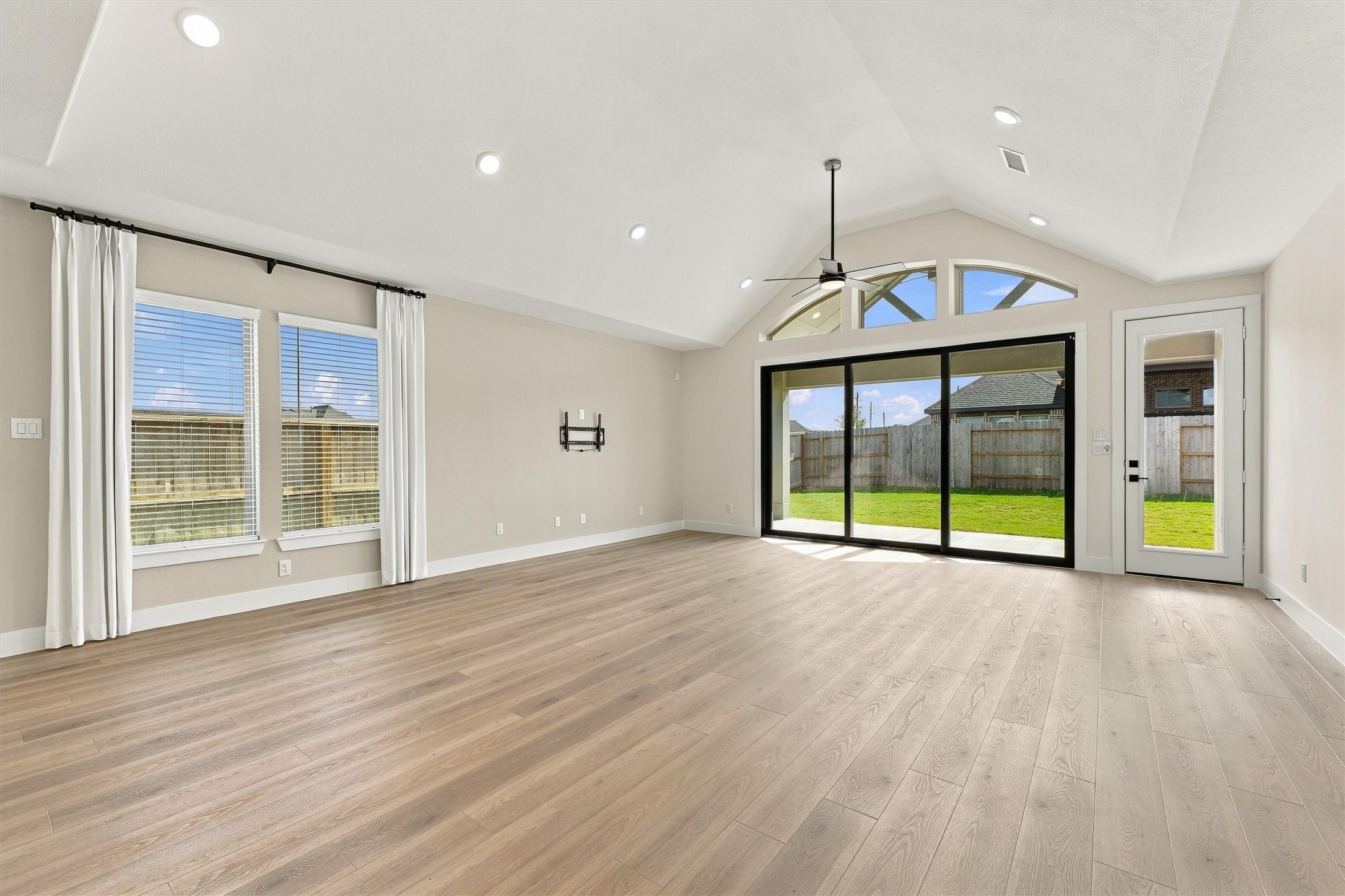 Vaulted ceilings and arched transom windows rise above multi-slide glass doors that open to the covered patio for seamless indoor-outdoor entertaining.