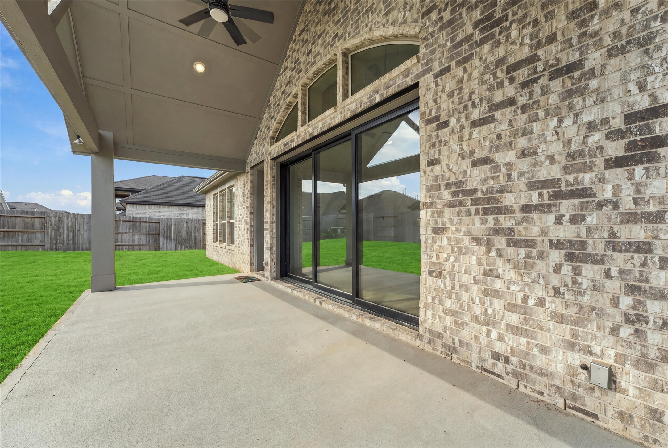 A gabled patio with a ceiling fan and recessed lighting sits under arched transom windows, and multi-slide glass doors open it to the living room.