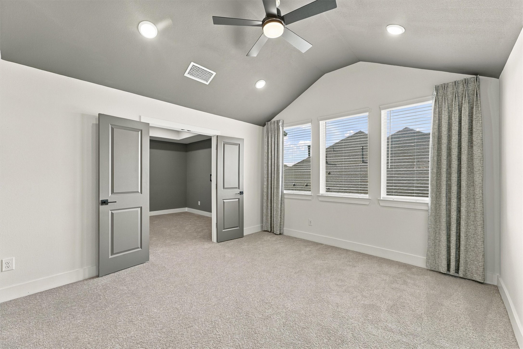 A vaulted game room with a ceiling fan, recessed lighting, and a wall of windows. Double doors open to the media room.