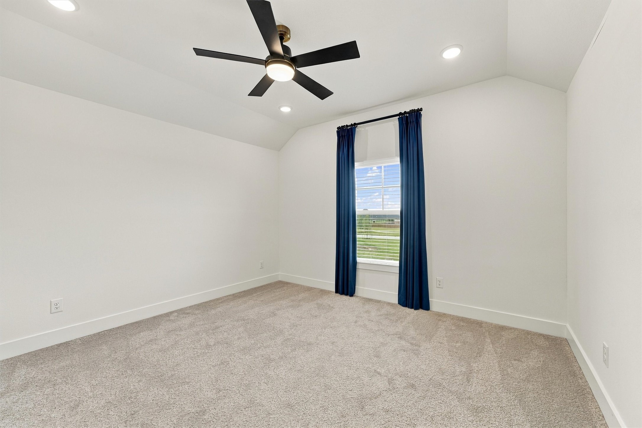 A vaulted bedroom with a ceiling fan, recessed lighting, and tailored navy drapery.